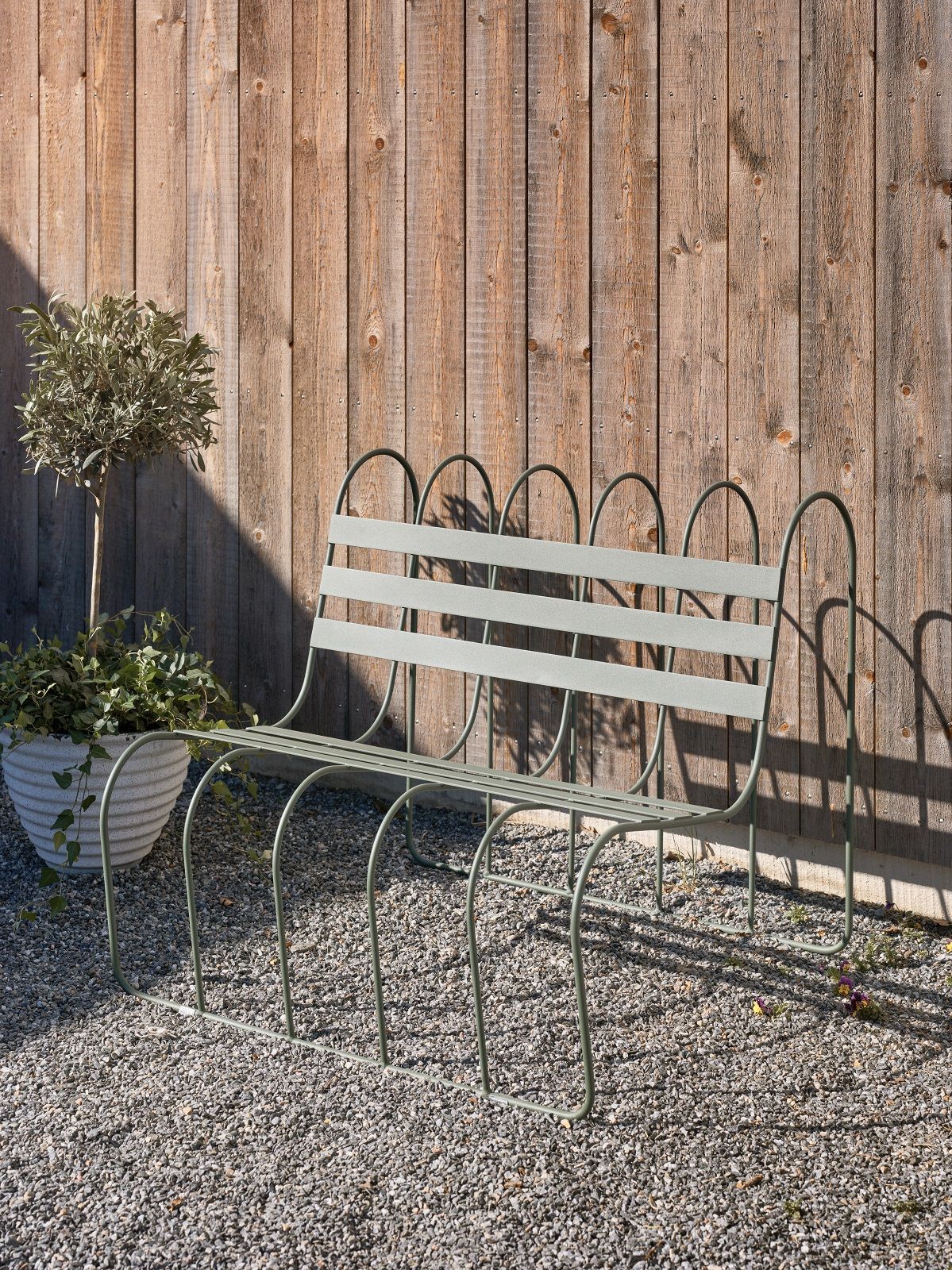 Gardener's Sofa von Design House Stockholm: Grüne Gartenbank aus Metall vor Holzwand.