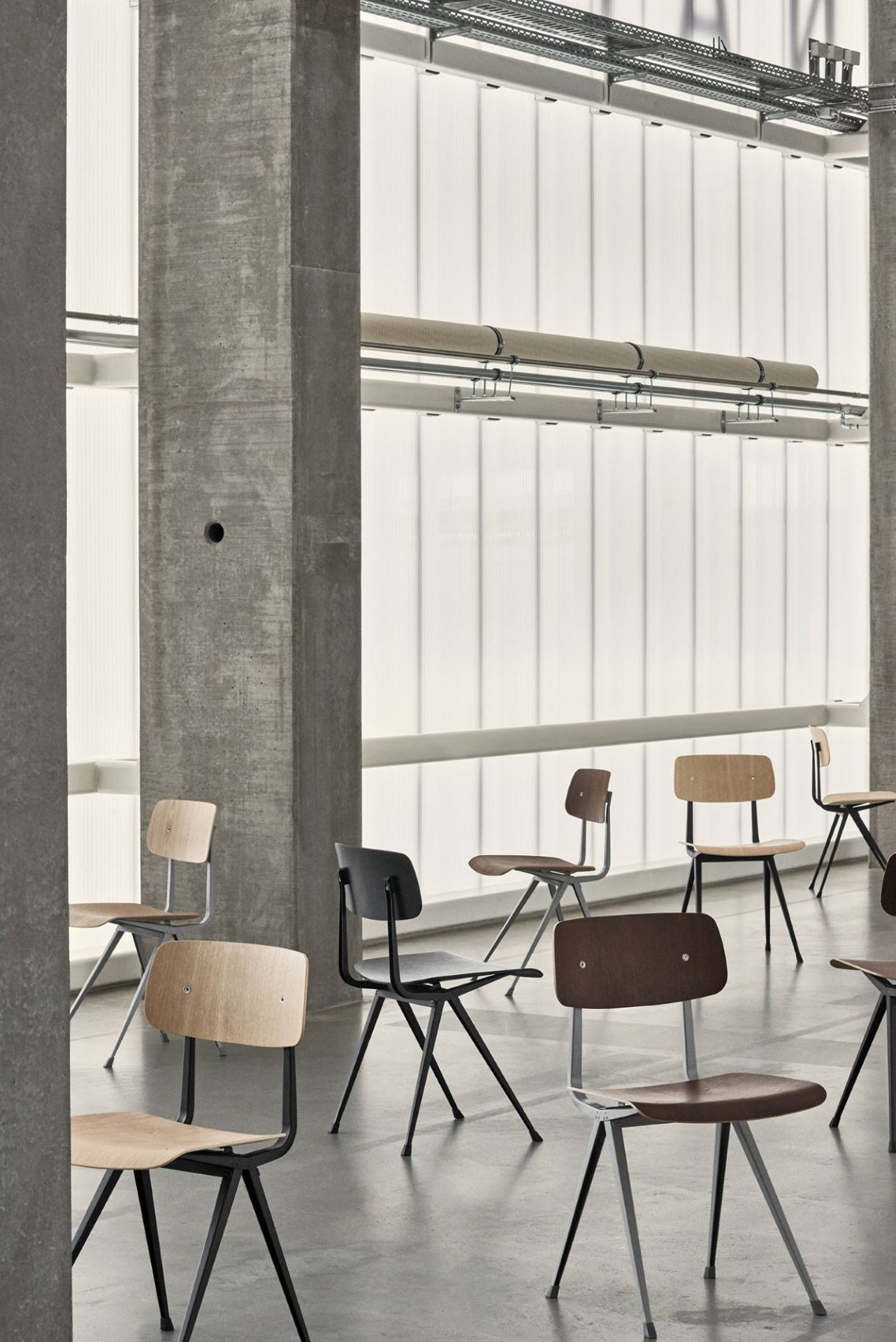 Mehrere Hay Result Chairs Stühle in verschiedenen Farben in einem modernem Raum mit Betonpfeilern und Fensterfront.