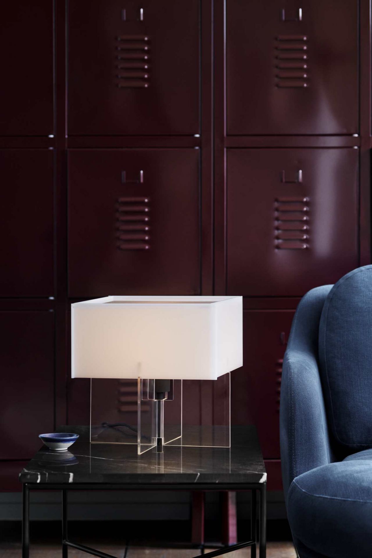 Nahaufnahme einer modernen Tischleuchte mit quadratischem Schirm und blauem Sofa im Hintergrund.
