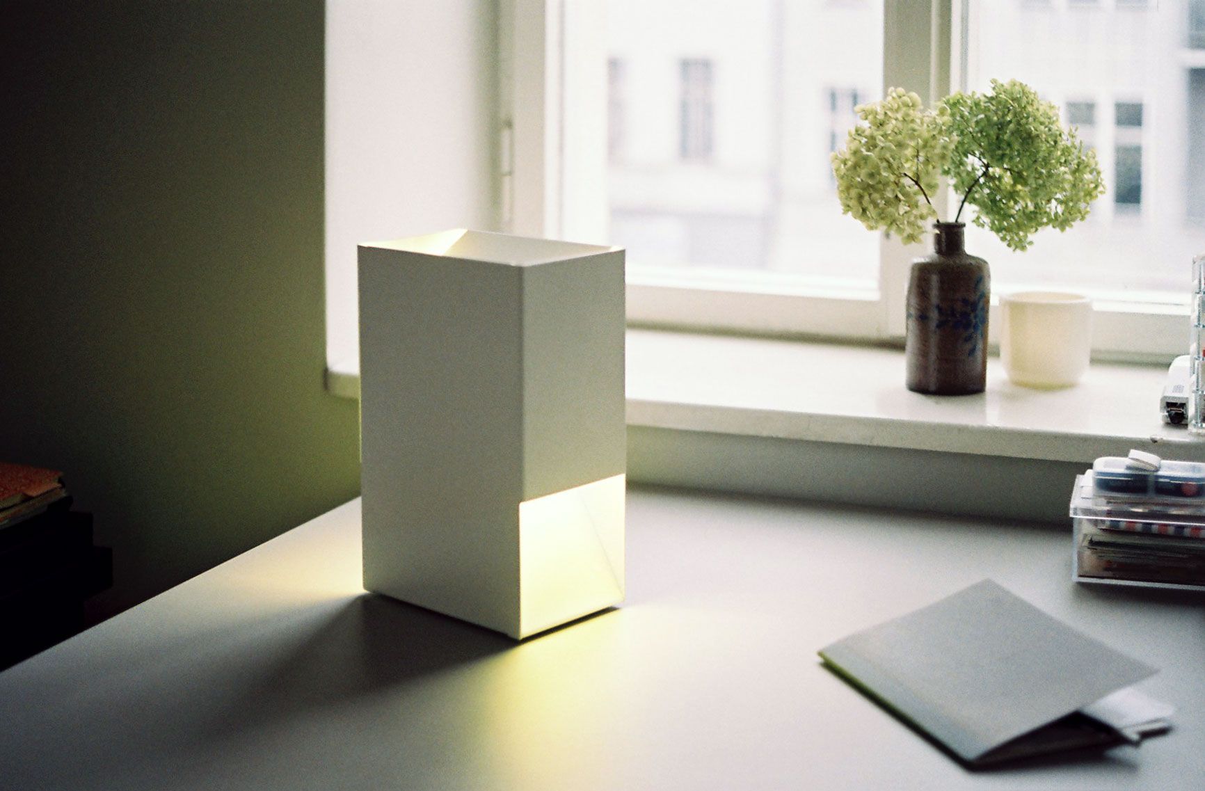 Weiße Linea1 Tischleuchte von Müller Möbelwerkstätten auf einem Schreibtisch, minimalistisches Design, stimmungsvolle Beleuchtung.