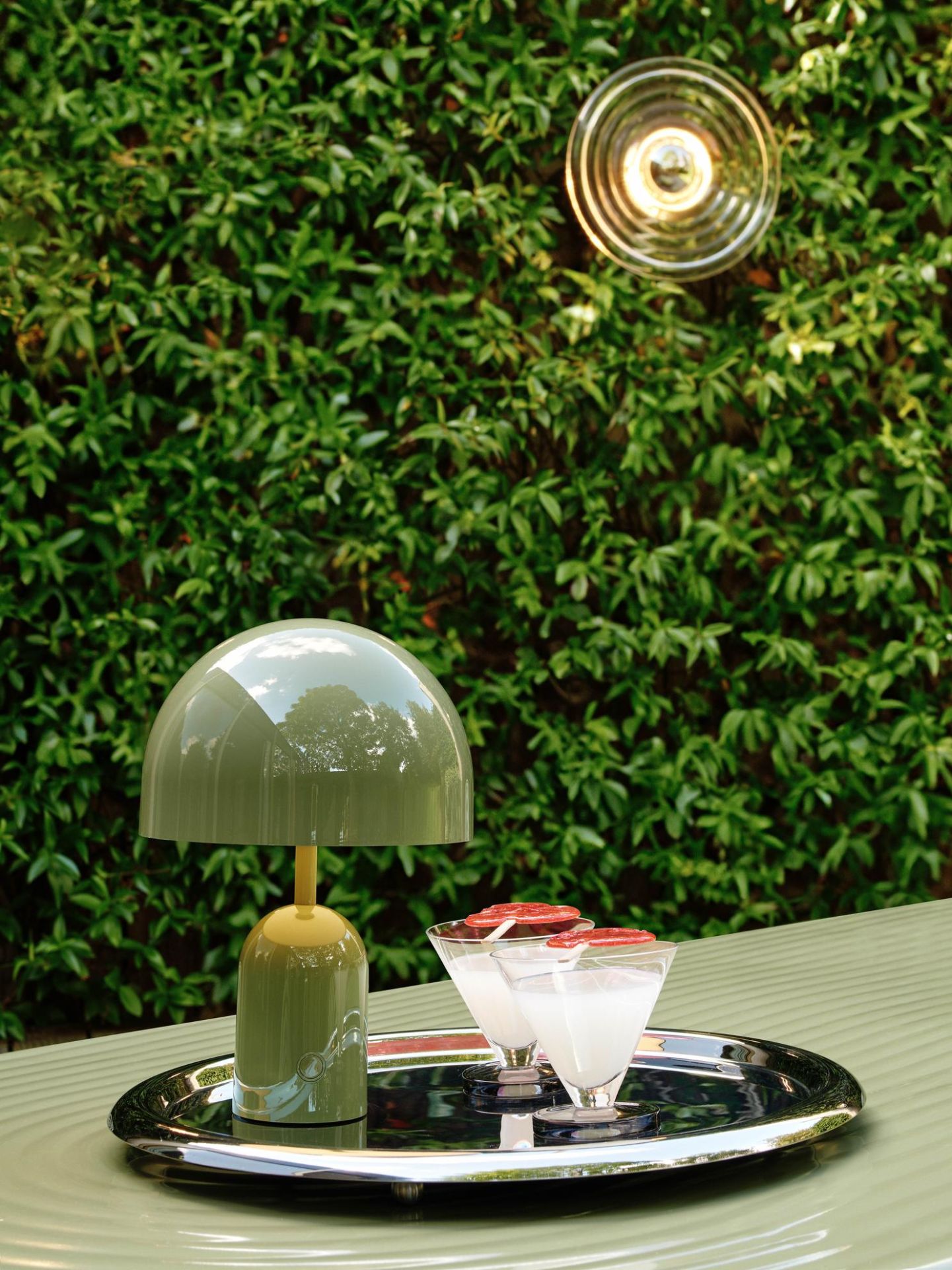 Grüne Tom Dixon Bell Akkuleuchte auf Tablett mit Cocktails vor grüner Wand.