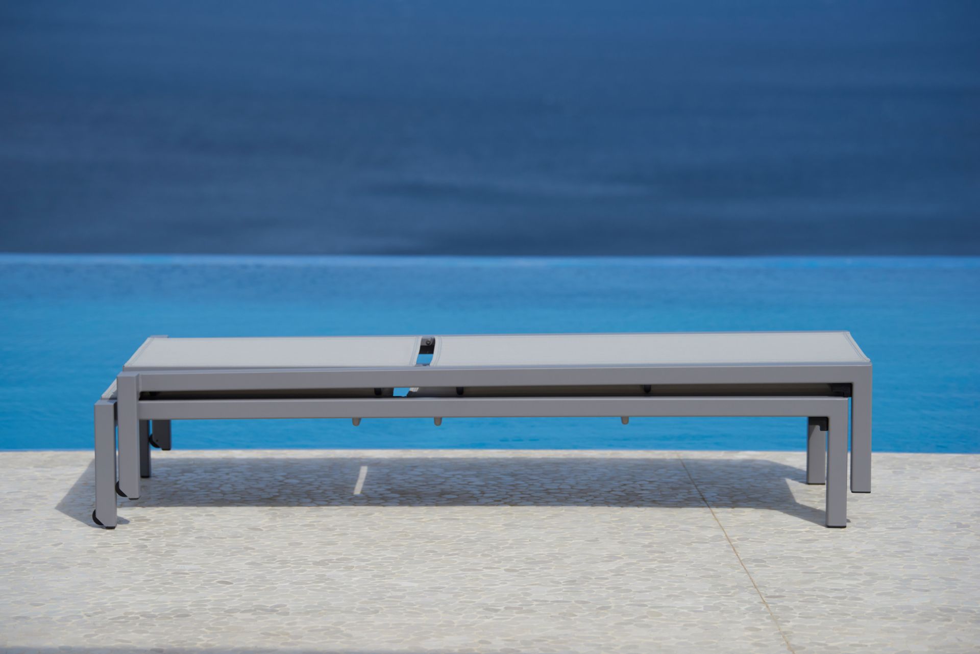 Stapelbare Cane-Line Sonnenliege "Relax Outdoor" in Grau vor blauem Pool und Meer.
