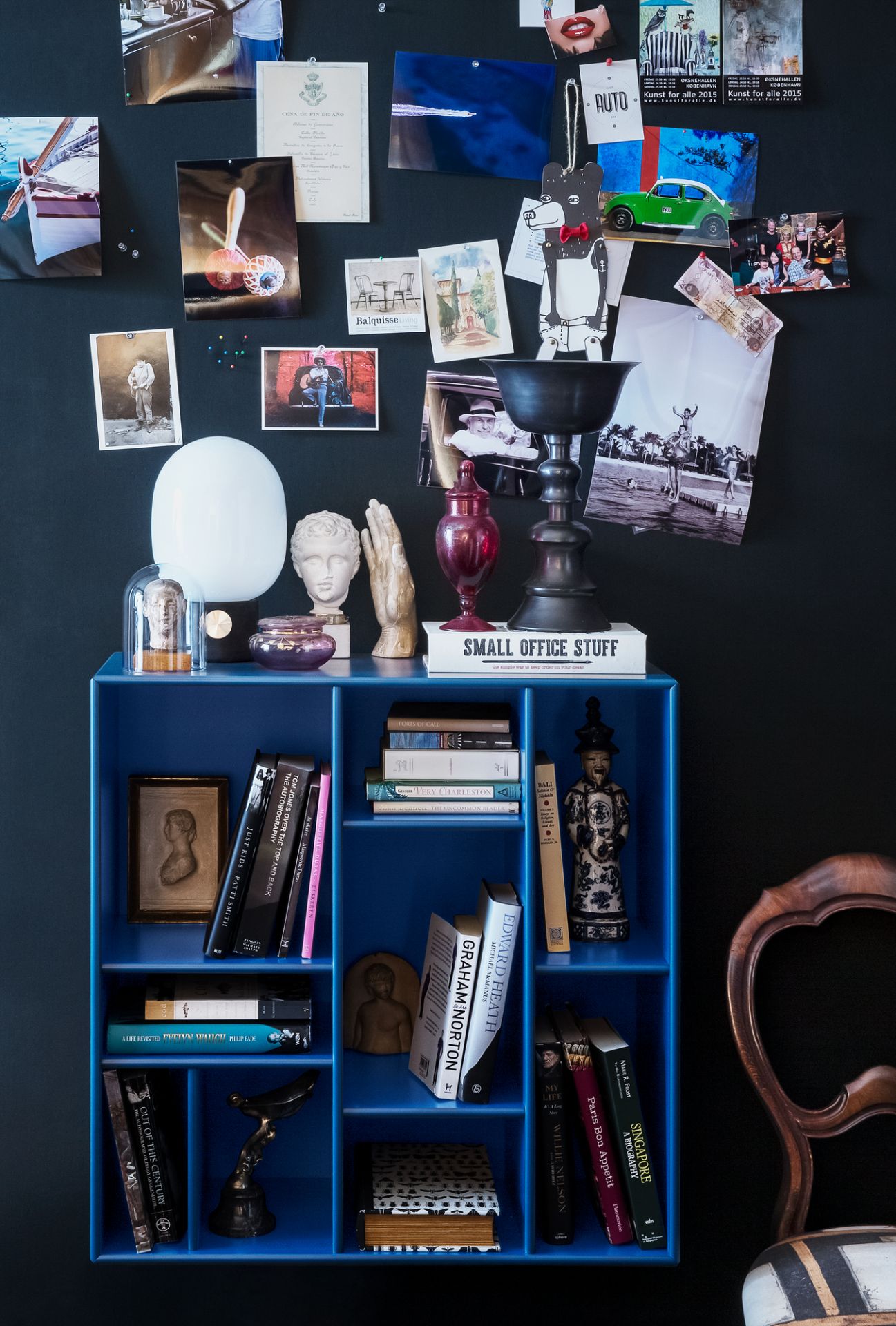 Blaues Compile Wandregal von Montana, gefüllt mit Büchern und Deko-Objekten vor schwarzer Wand.