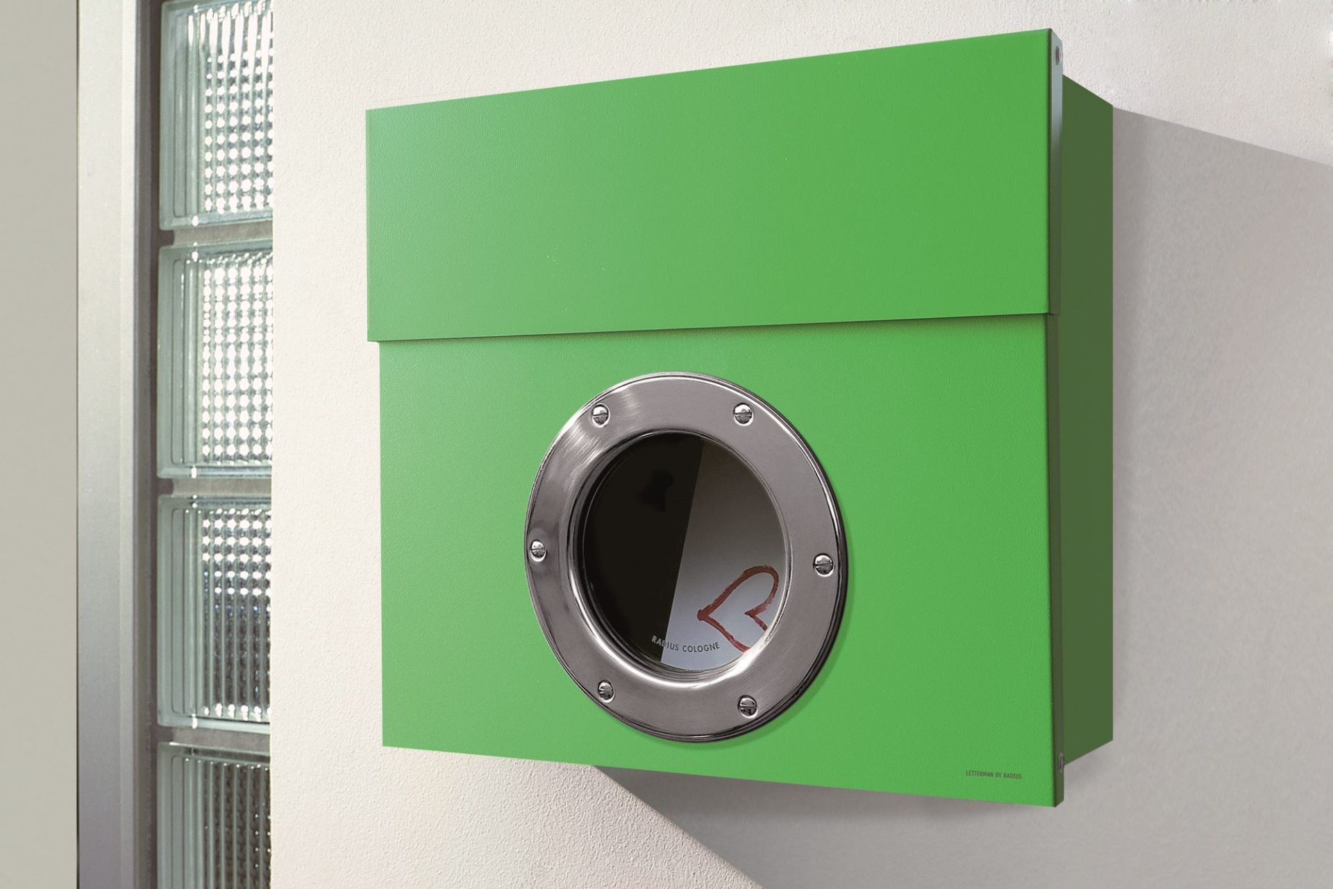 Grüner Letterman Briefkasten mit Bullauge und Edelstahlring an einer weißen Wand. Moderner Design-Briefkasten.