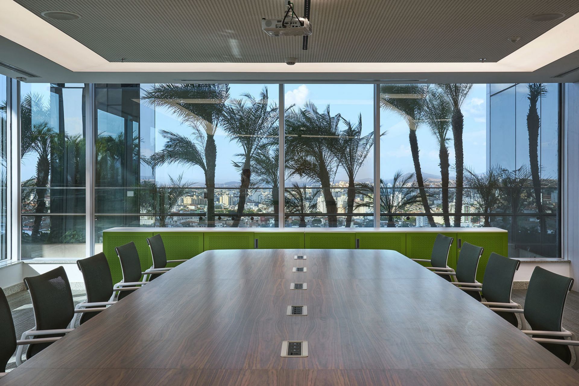 Konferenzraum mit langem Holztisch und Vitra Physix Studio Bürostühlen vor Panoramafenster mit Palmen.