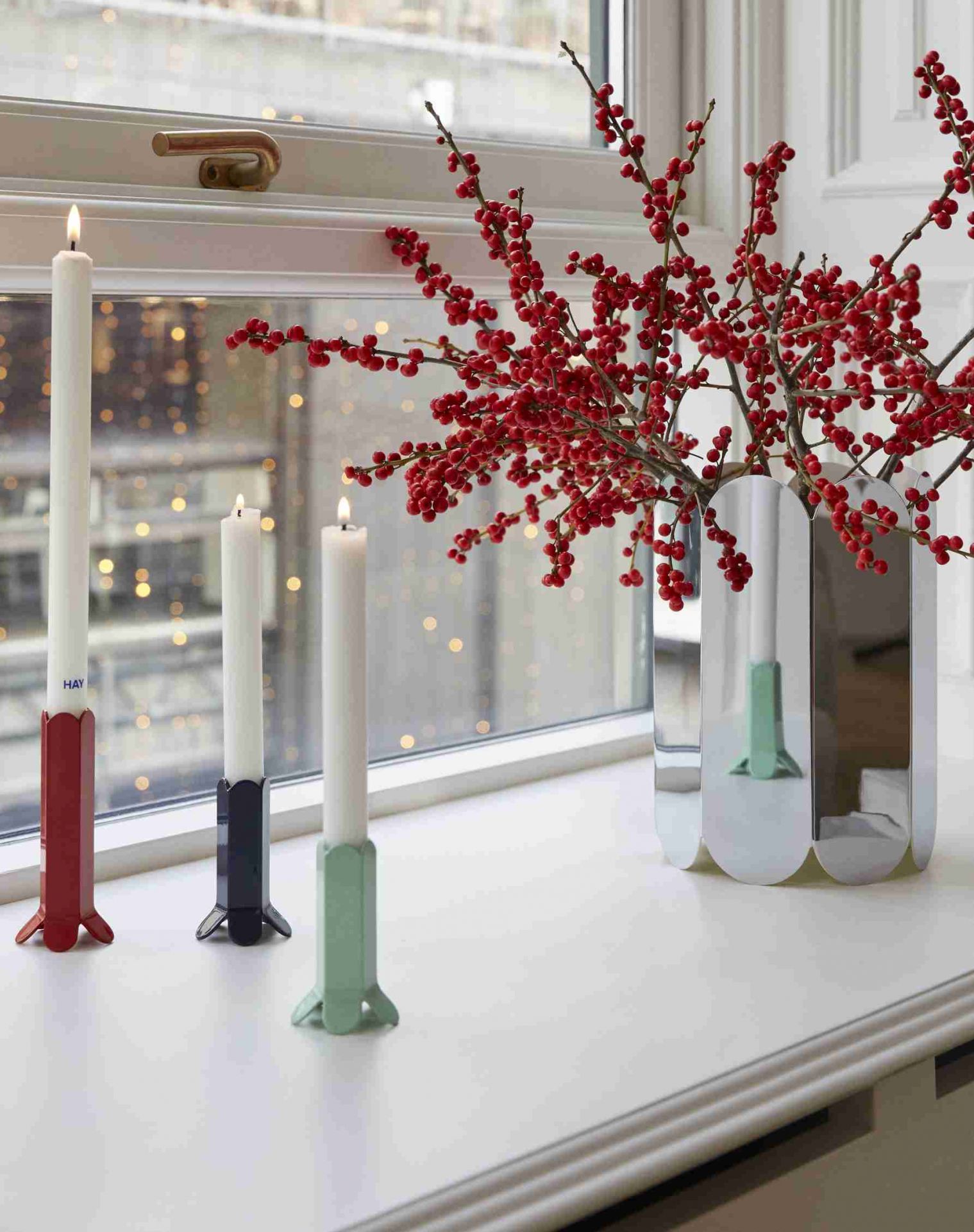 HAY Arcs Vase L Mirror: Silberne Design-Vase mit roten Beeren und Kerzenständern auf einer Fensterbank.