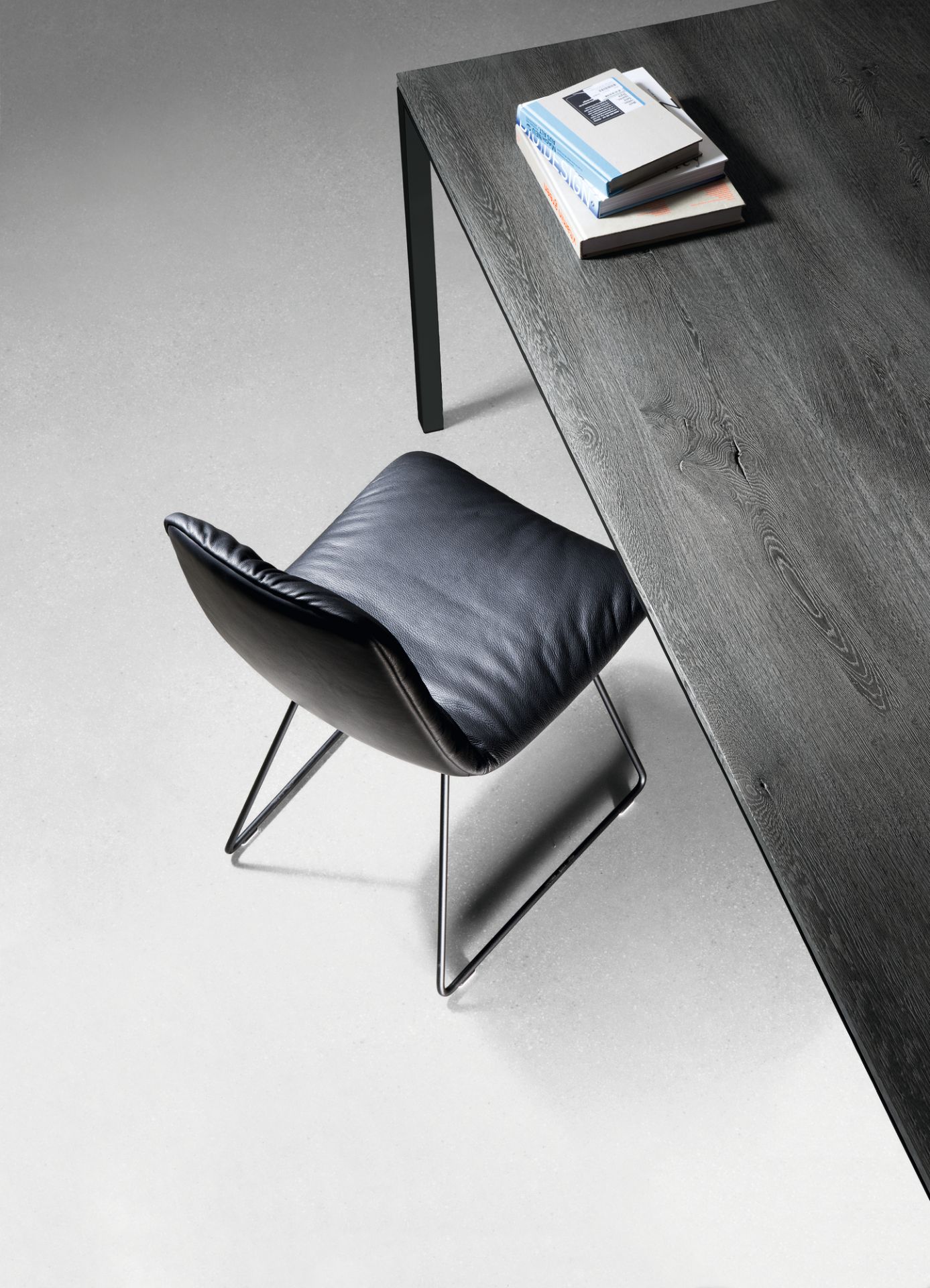 Detailaufnahme vom Janua S 600 Tisch Eiche geköhlt mit schwarzem Lederstuhl und Büchern.