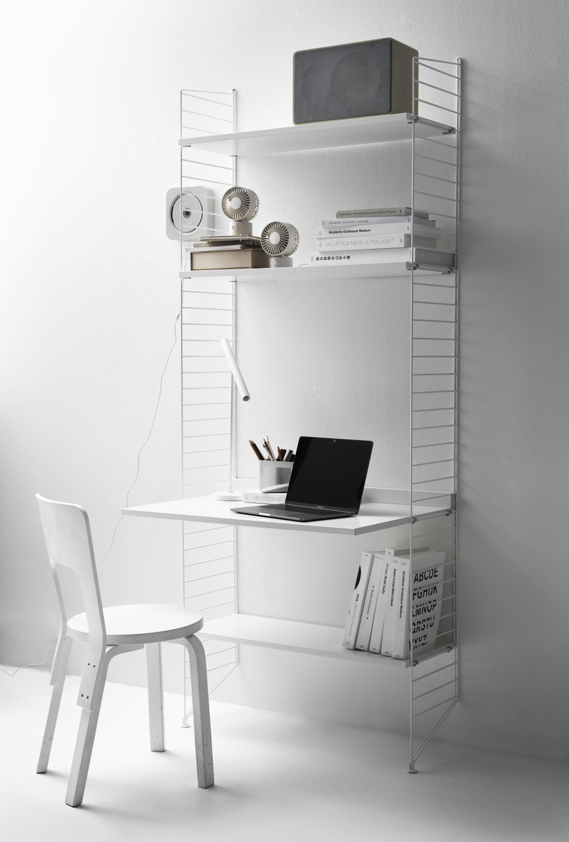 Heller Arbeitsplatz mit String Furniture Regalsystem, Schreibtisch, Laptop und weißem Stuhl. Modernes Design.