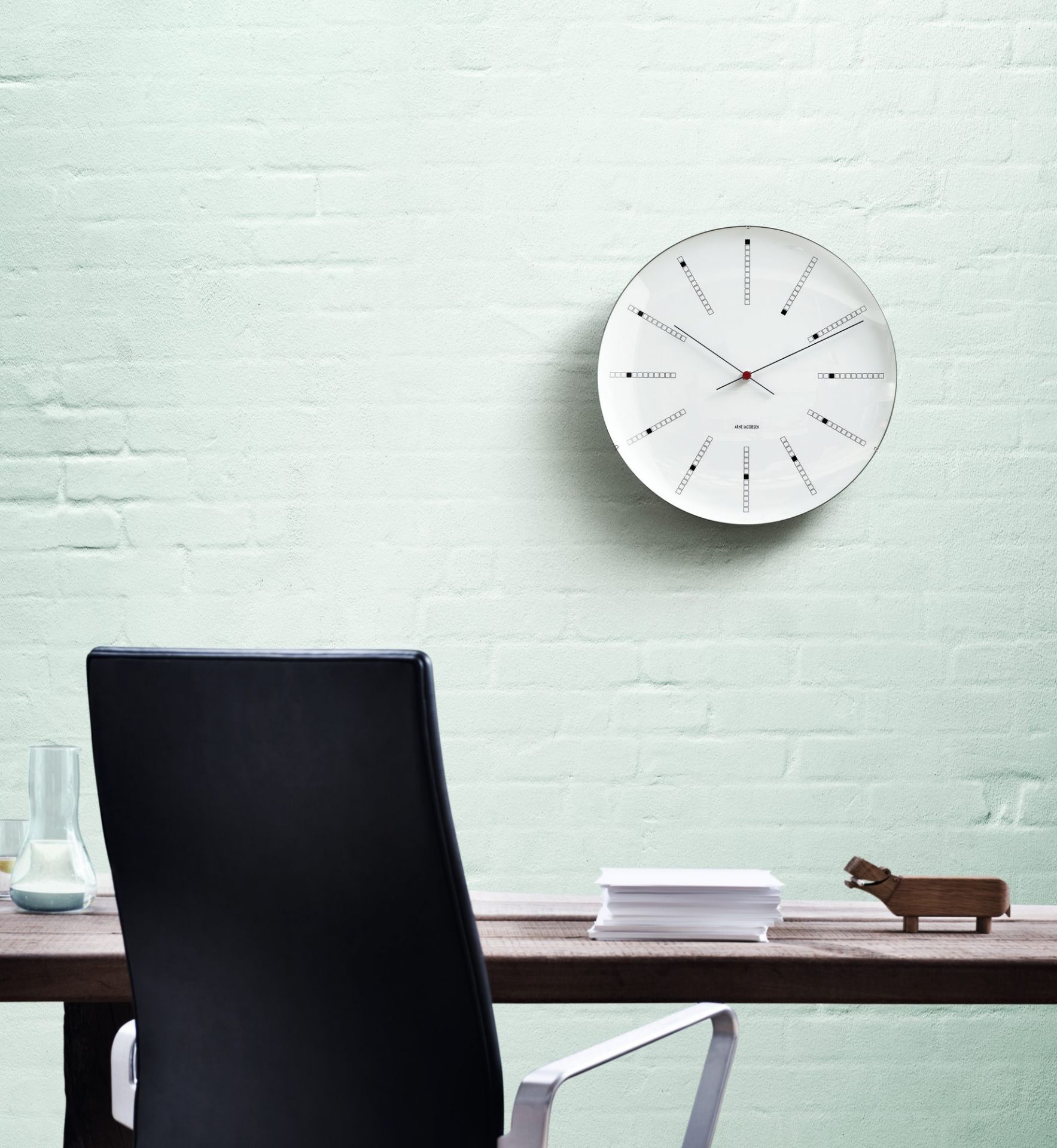 Weiße Bankers Wanduhr von Rosendahl Timepieces an einer hellgrünen Ziegelwand im Büro.