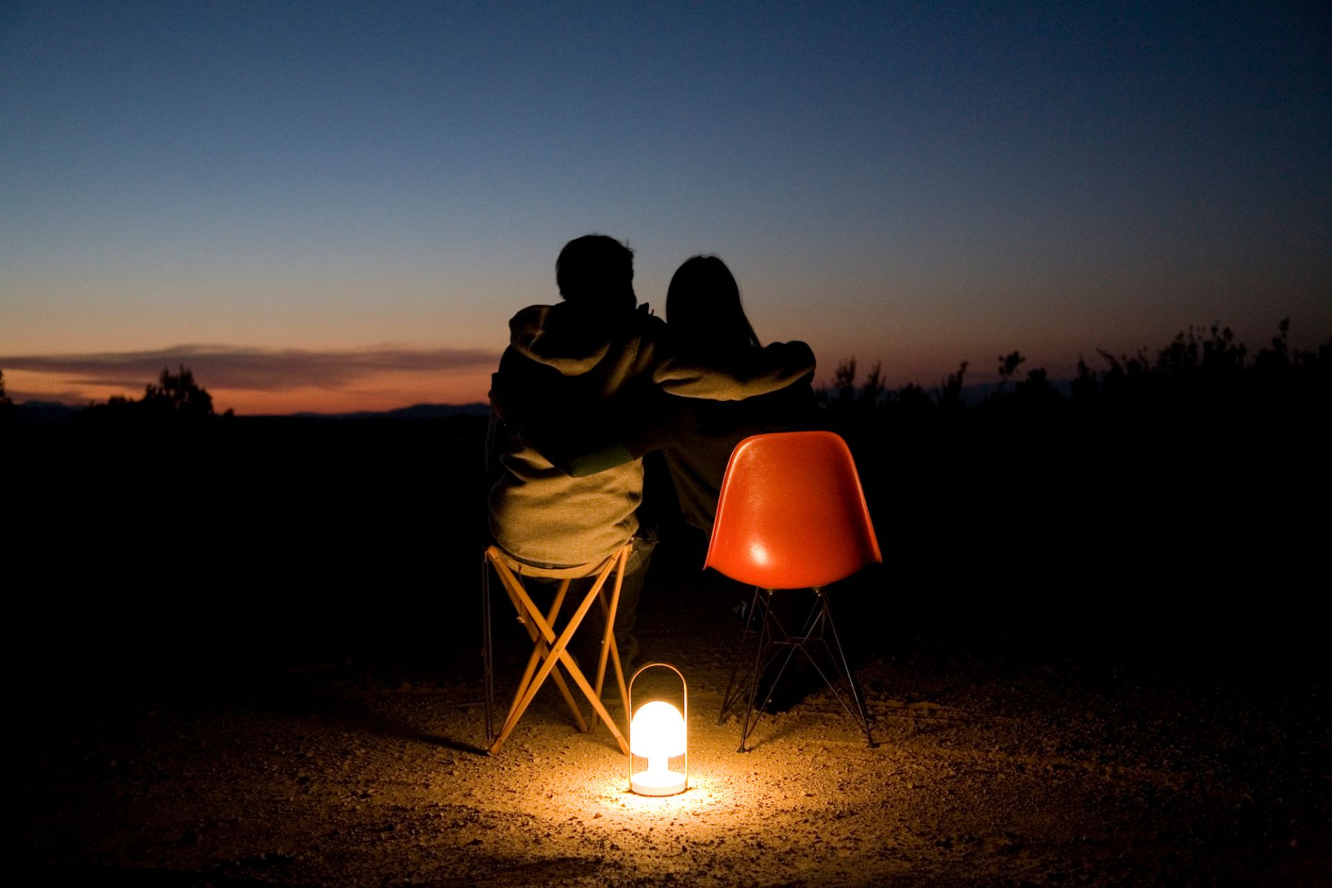 Paar sitzt im Dunkeln bei Sonnenuntergang, beleuchtet von der FollowMe LED Akkuleuchte in Terrakotta.