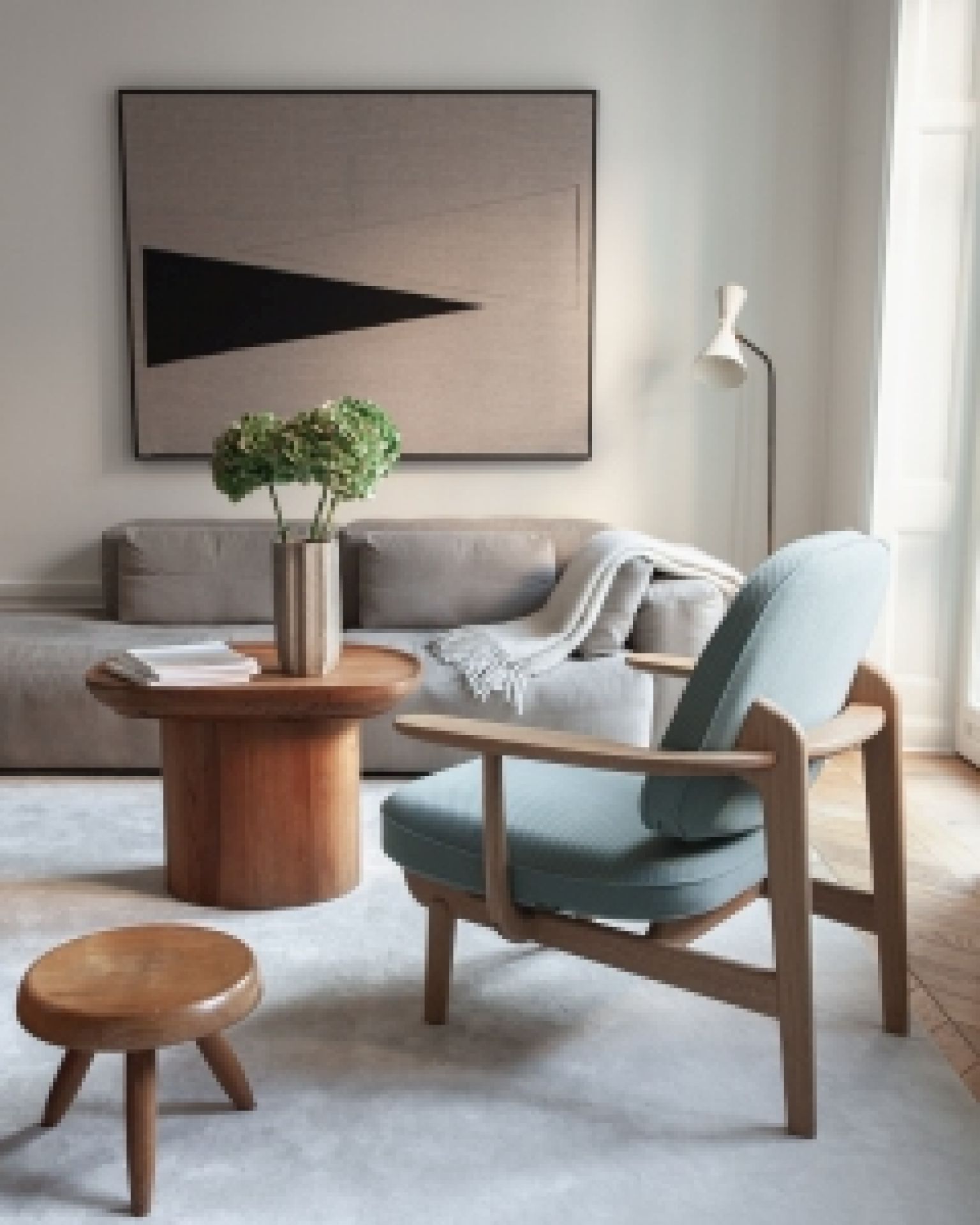 Heller Wohnraum mit blauem Fred Sessel von Fritz Hansen, Holztisch und Kunstwerk an der Wand.