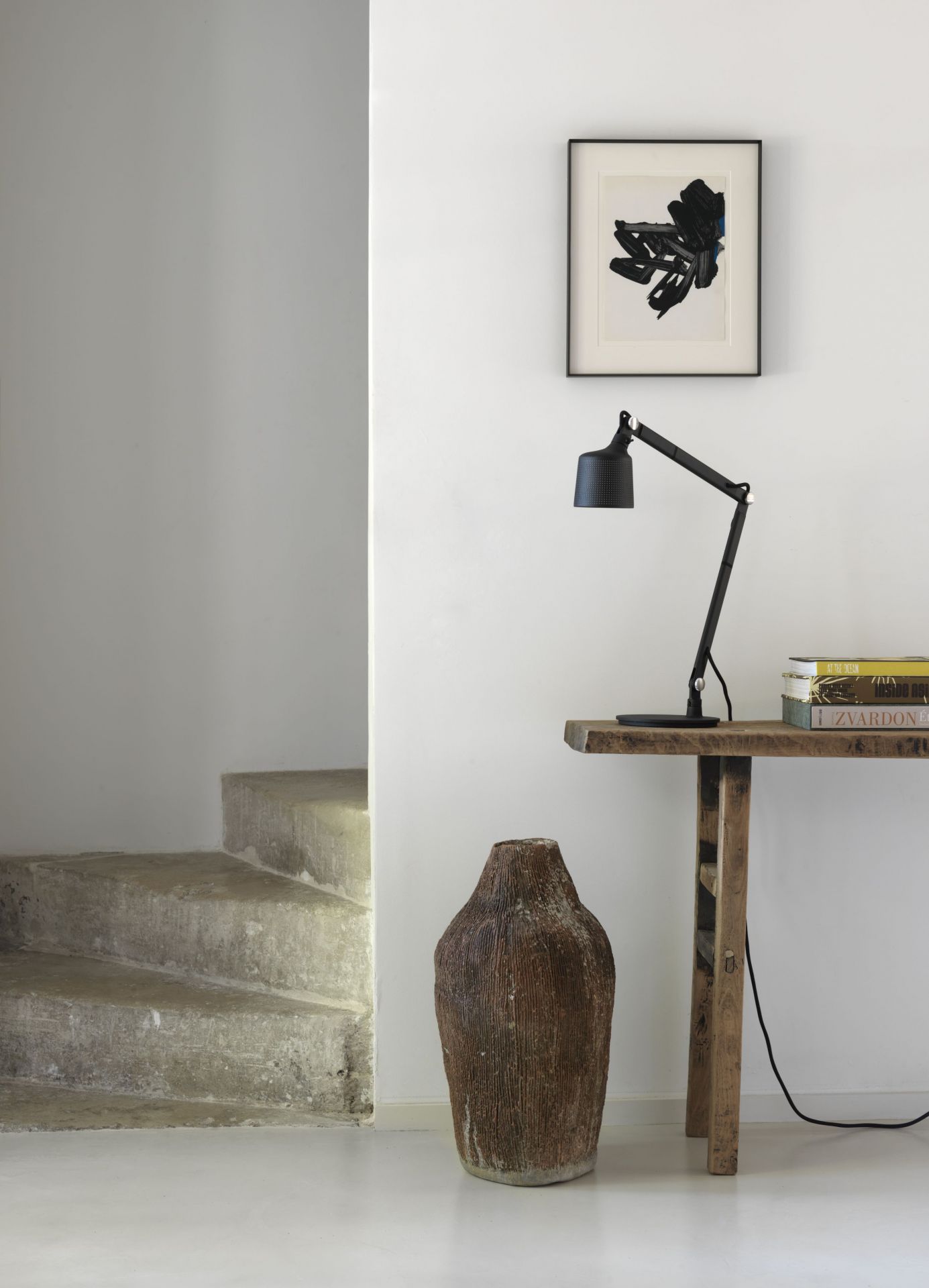 Schwarze Vipp Tischlampe auf rustikalem Holztisch mit Büchern und dekorativer Vase, minimalistisches Interieur mit Treppe.