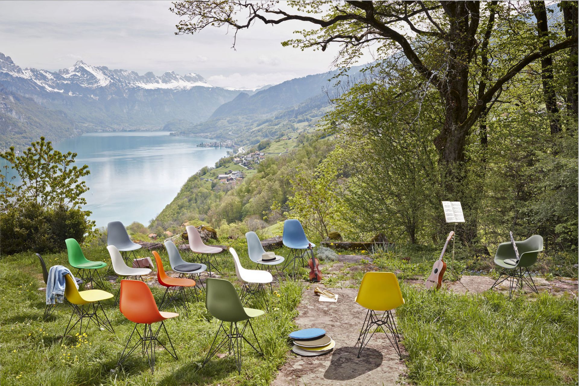 Bunte Eames Plastic Arm Chairs DAR Stühle von Vitra im Grünen mit Bergpanorama und See.