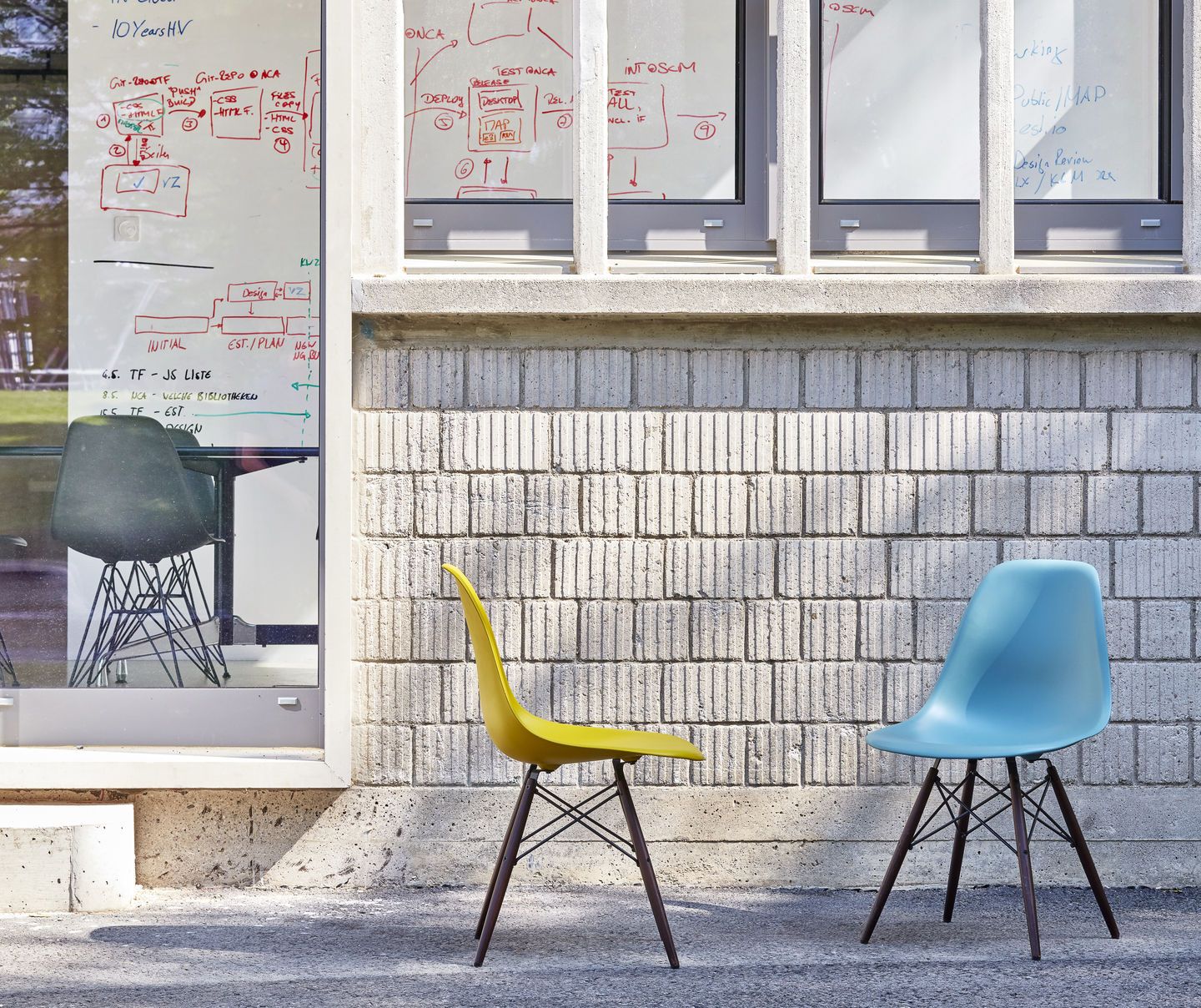 Drei Eames Fiberglass Chairs DSW von Vitra in Gelb, Blau und Grau vor Bürowand.
