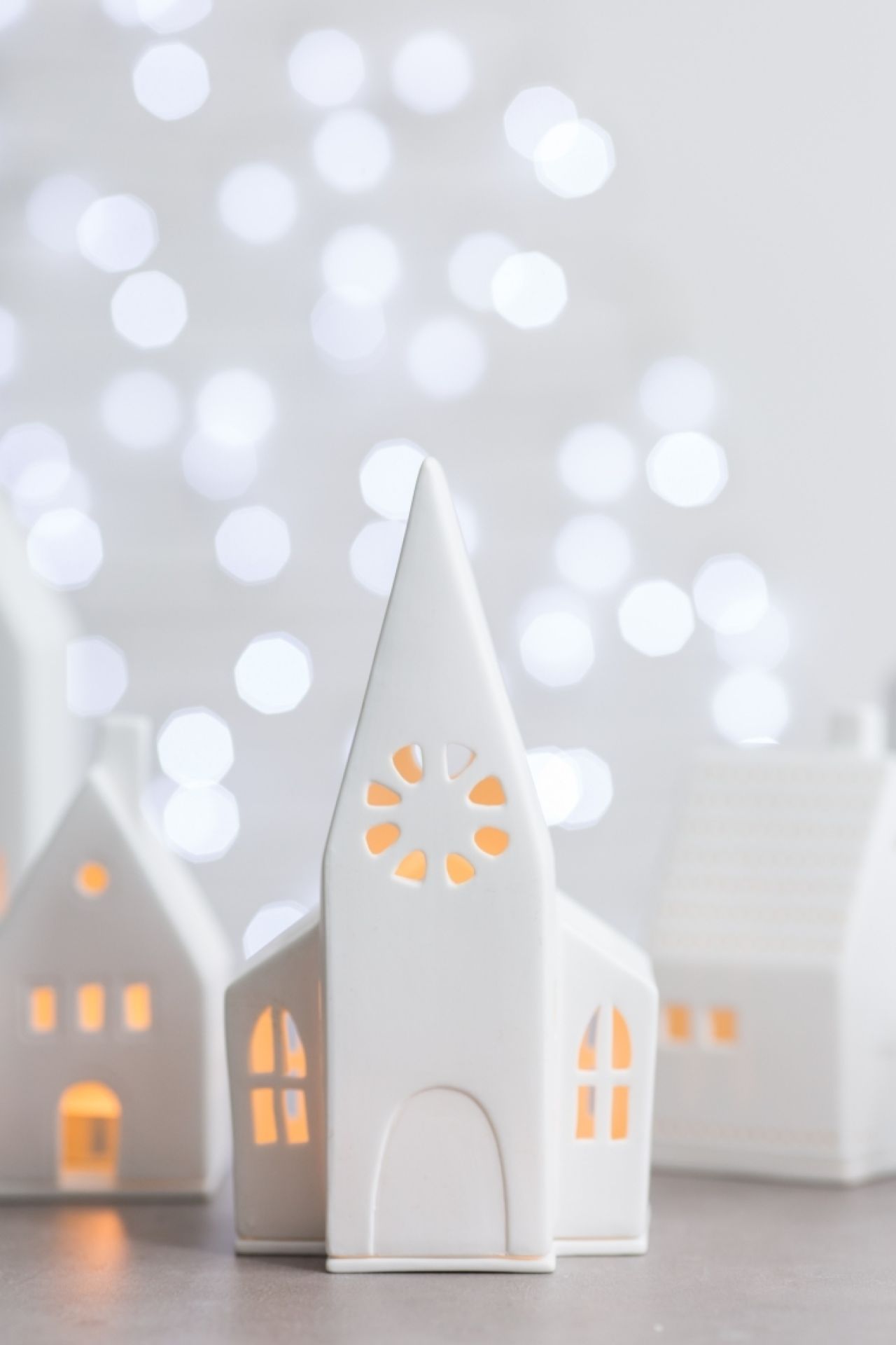 Weißes Lichthaus in Kirchenform mit warmem Licht und Bokeh im Hintergrund. Dekorative Häuser für Weihnachten.
