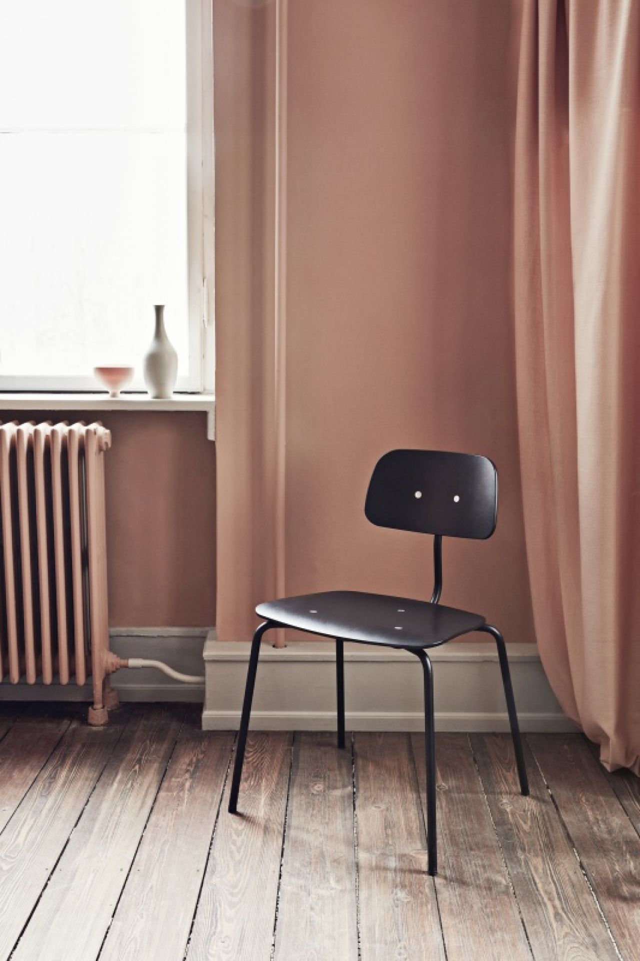 Schwarzer Kevi 2060 Stuhl mit Stahlgestell vor rosa Wand und Holzboden, minimalistisches Design.