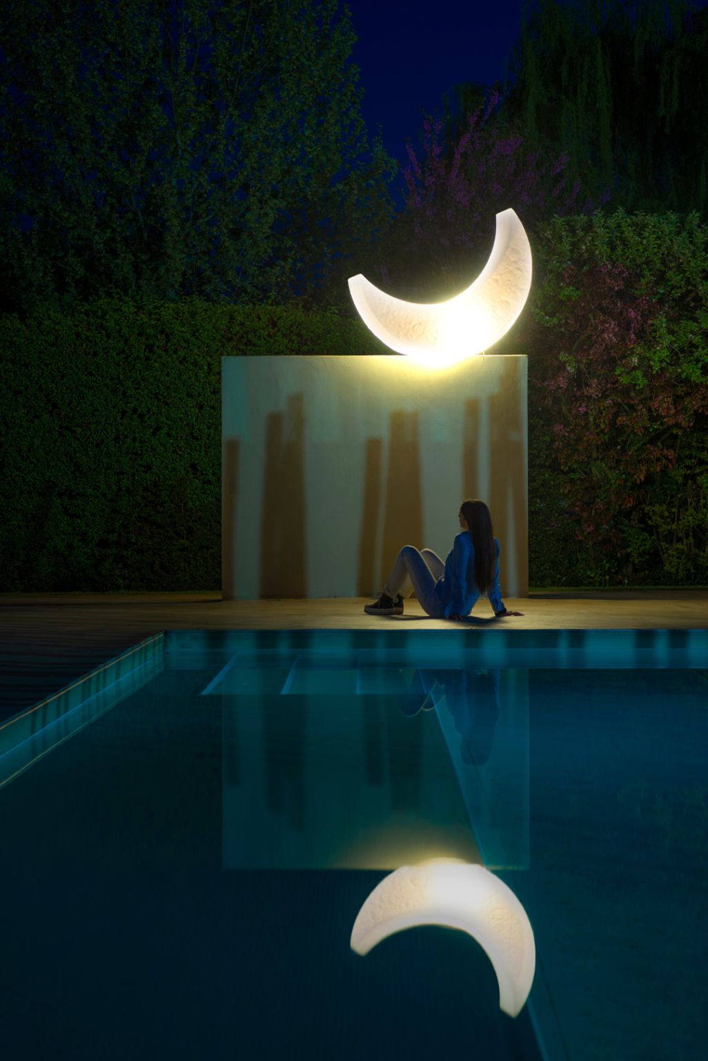 Frau sitzt am Pool mit beleuchteter My Moon Lampe von Seletti im Garten bei Nacht.