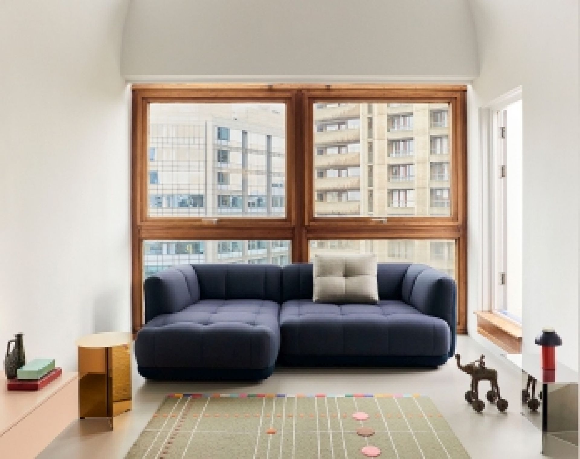Blaues Quilton Sofa von Hay vor einem Fenster mit Blick auf die Stadt.