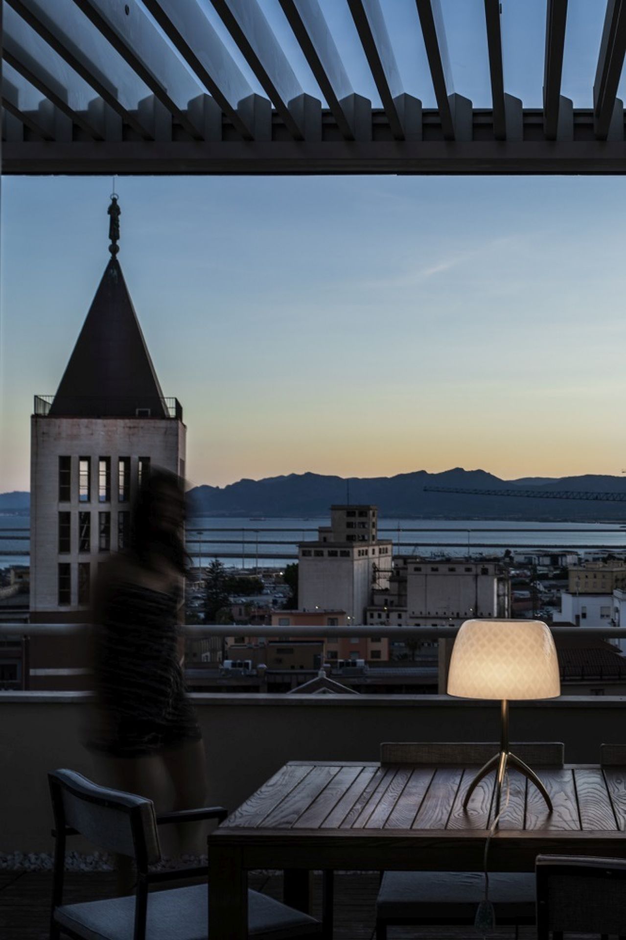 Lumiere Tischleuchte von Foscarini auf einem Holztisch mit Stadtblick im Hintergrund, stimmungsvolle Beleuchtung.