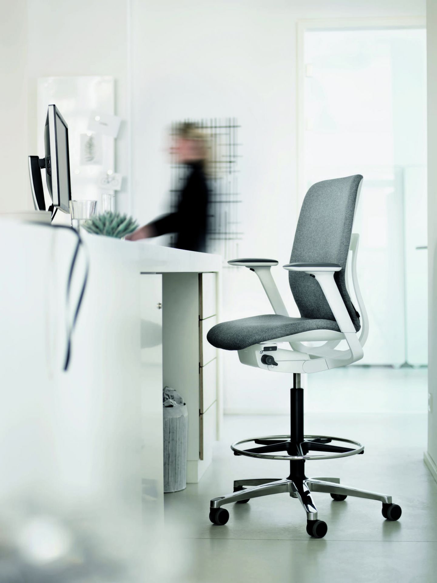 Ergonomischer Steh-Sitz-Stuhl mit grauem Bezug und weißem Rahmen für modernes Büro oder Homeoffice.