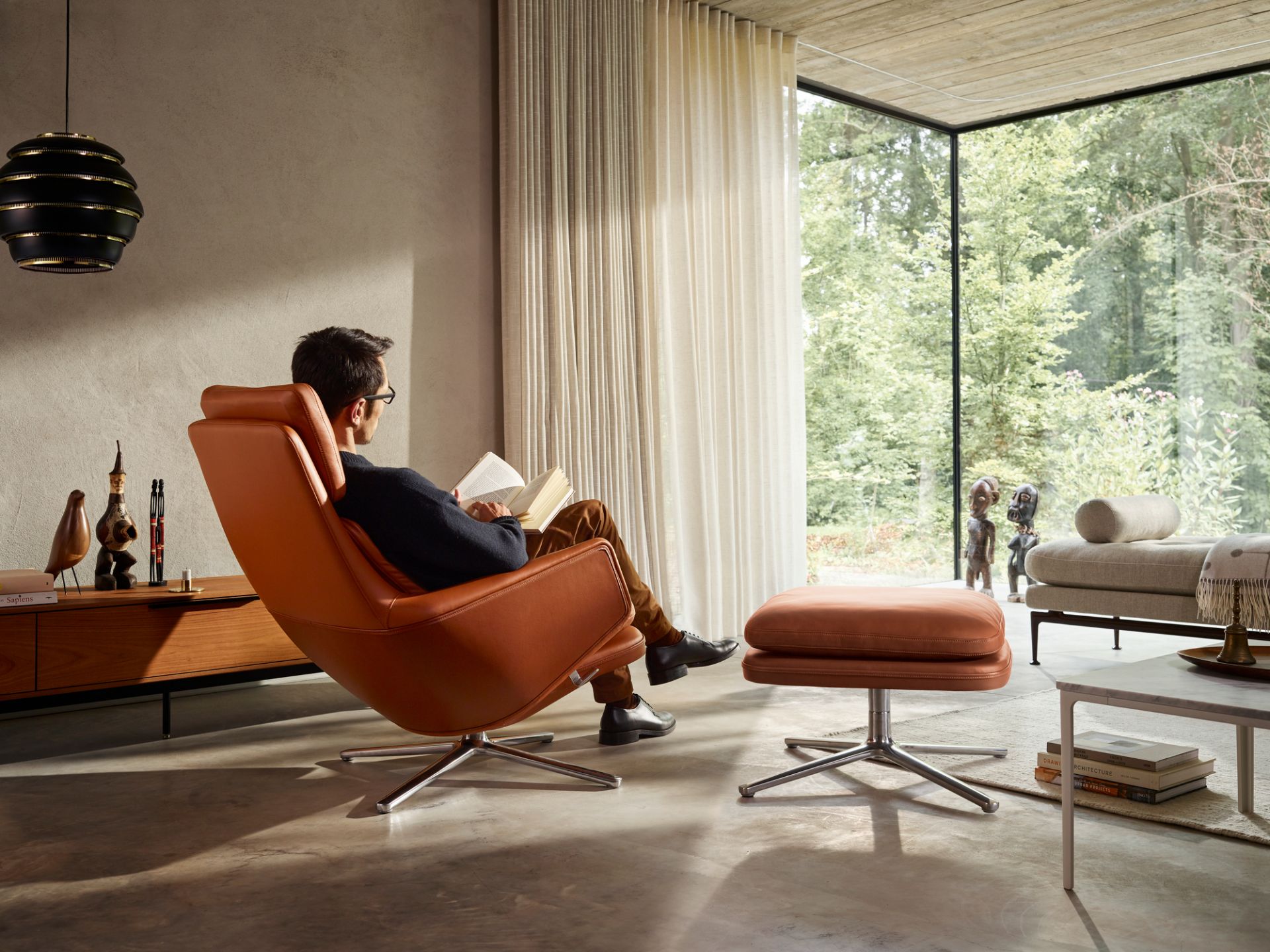 Mann liest im Vitra Grand Relax Sessel mit Ottoman in modernem Wohnzimmer.