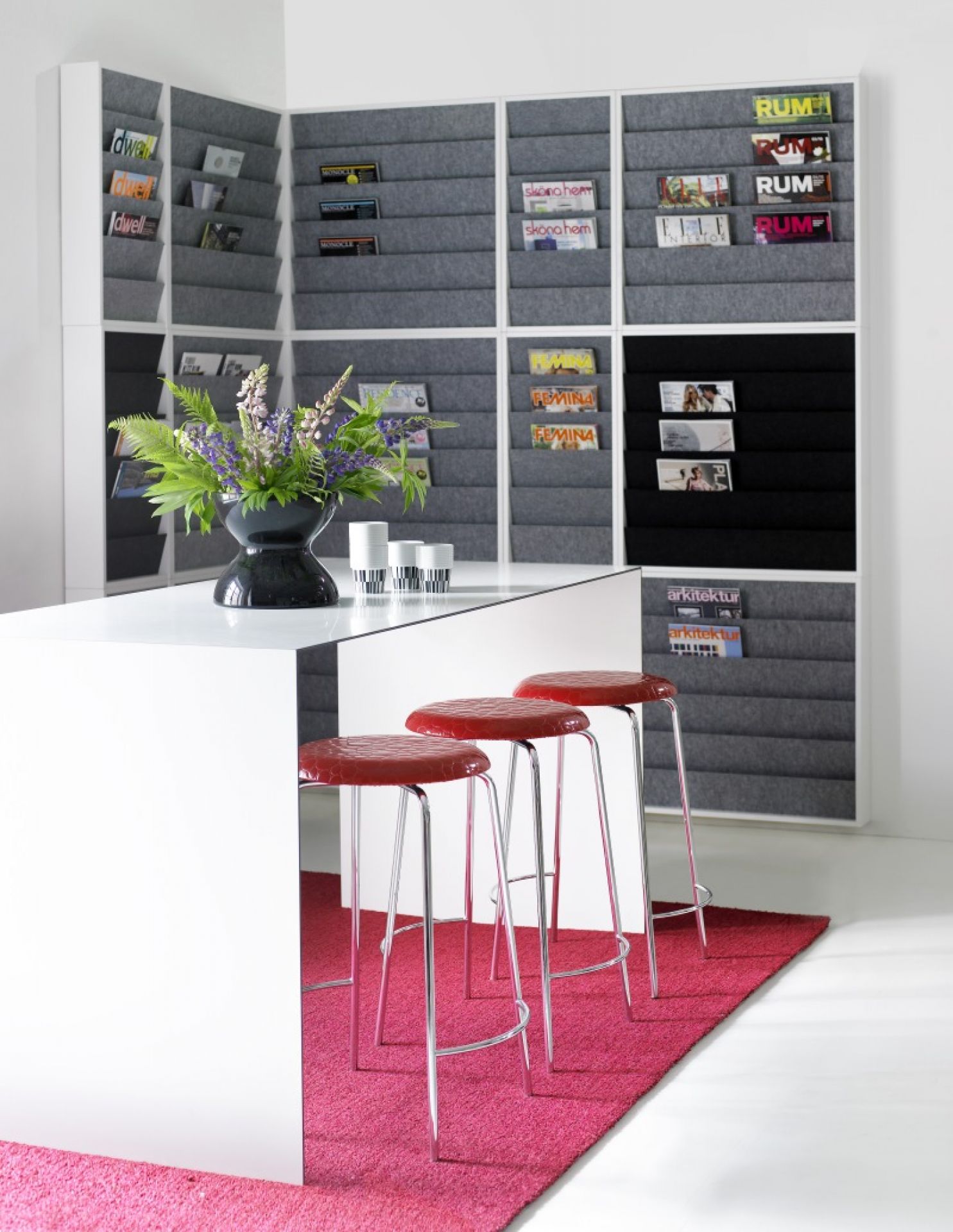 Heller Raum mit Karl Andersson & Soener Thinner Tisch, roten Barhockern und Zeitschriftenregal.