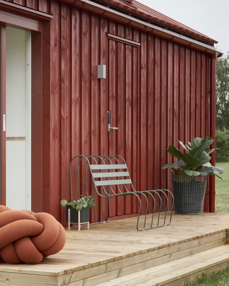 Gardener's Sofa von Design House Stockholm, grüne Outdoor-Metallbank mit Holzboden und roter Holzwand.