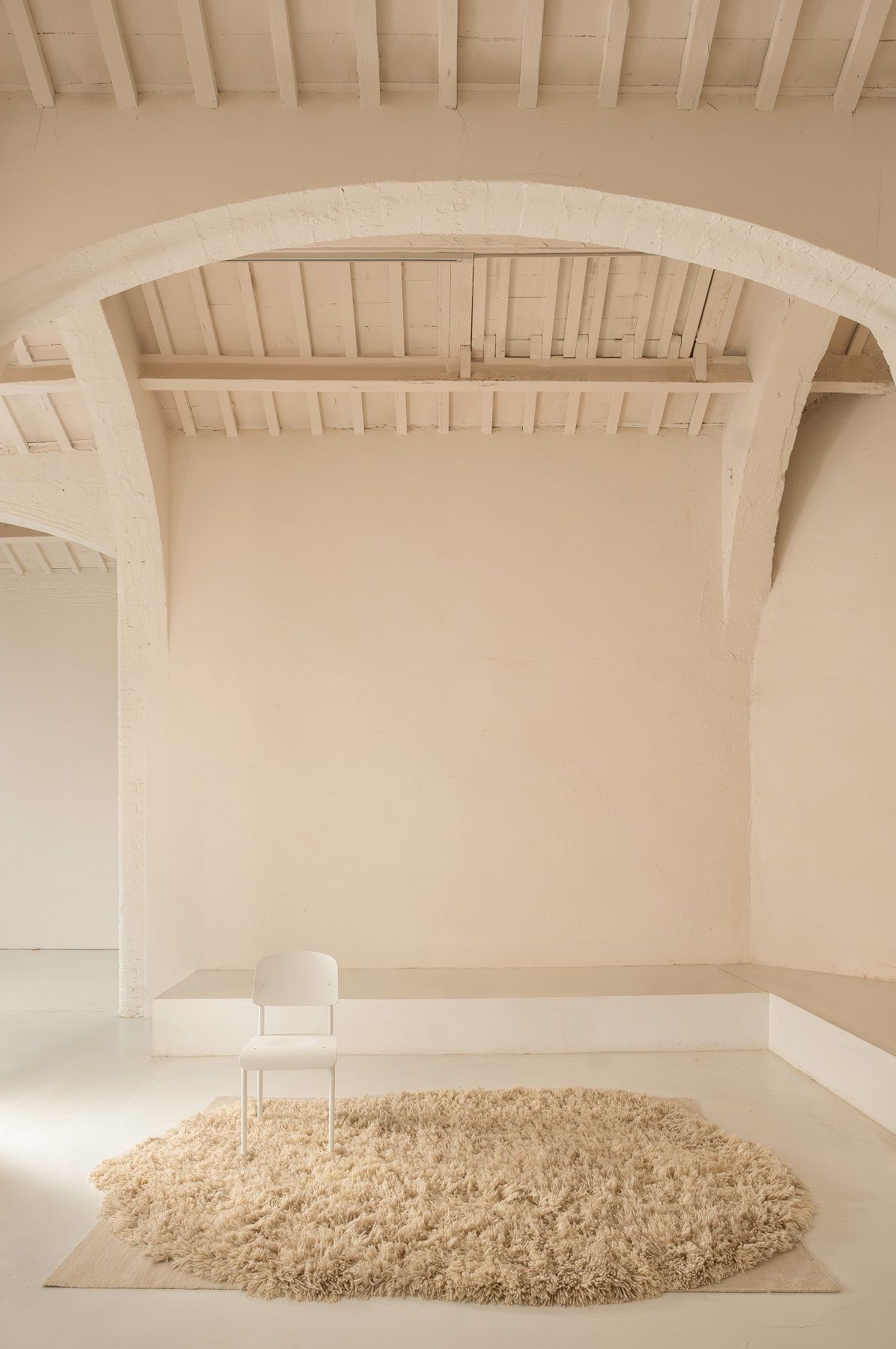 Nanimarquina Alga Rug Teppich in Beige mit Fransen und einem weißen Stuhl in minimalistischem Raum.