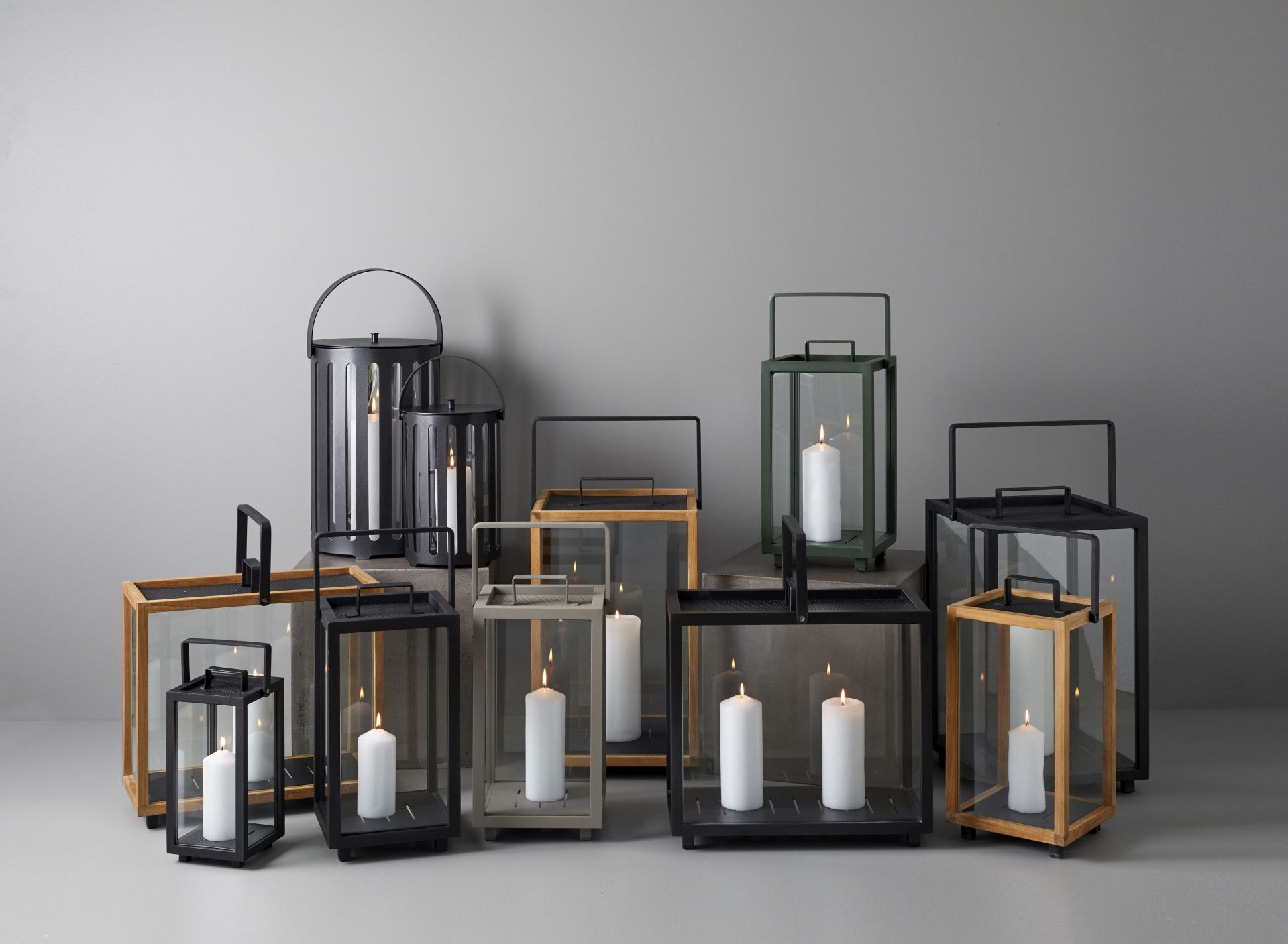 Eine Kollektion von Cane-Line Lighthouse Laternen aus Teakholz und Metall mit brennenden Kerzen.