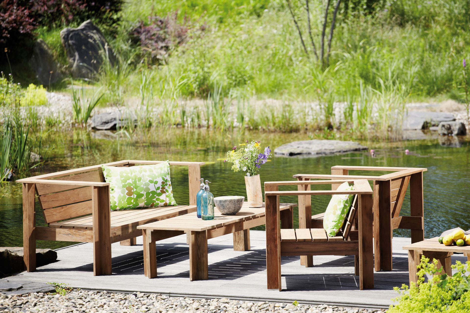Batten Loungesofa von Jan Kurtz aus Naturholz am See mit Kissen und Tisch.