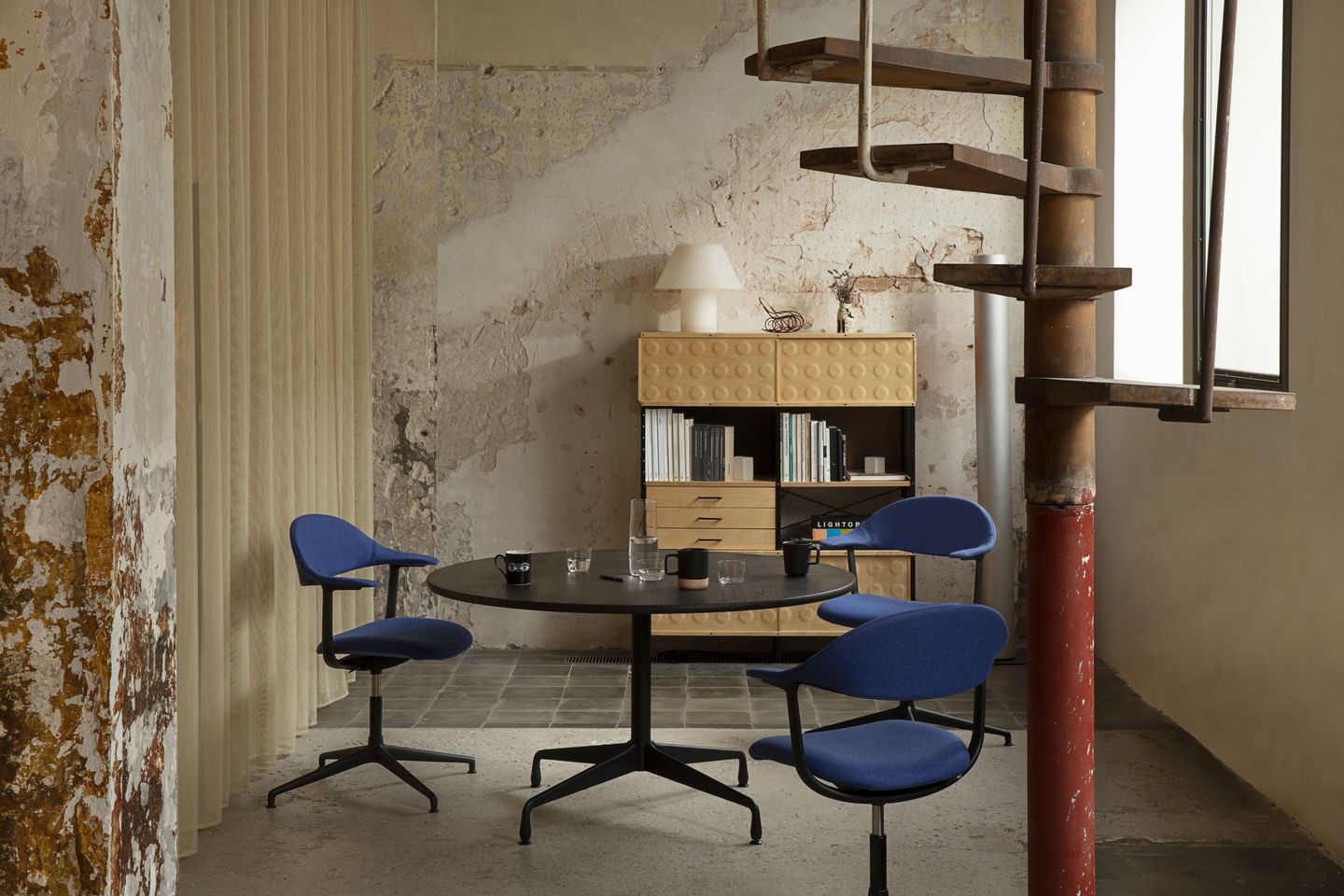 Mynt Bürodrehstühle von Vitra in blau um einen runden Tisch in einem Loft-Büro.