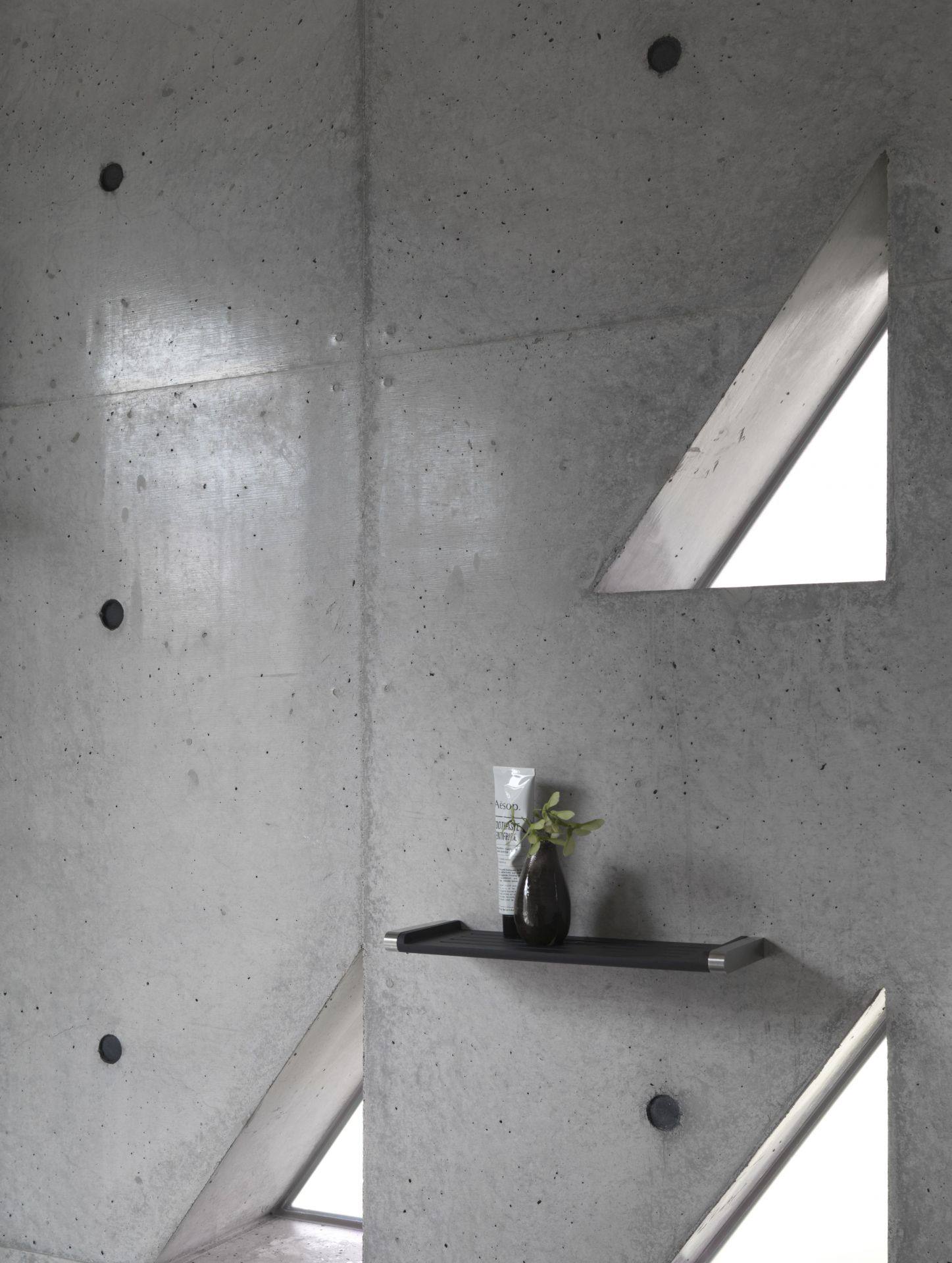 Schwarze Vipp Badablage an Betonwand mit Badutensilien und dreieckigem Fenster. Minimalistisches Badezimmer Design.