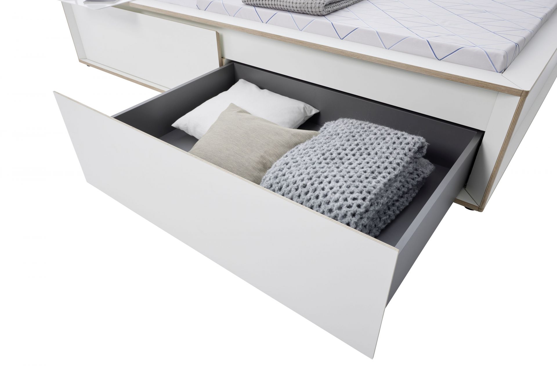 Spaze Bett von Müller Möbelwerkstätten mit offener Schublade, gefüllt mit Kissen und einer grauen Strickdecke.