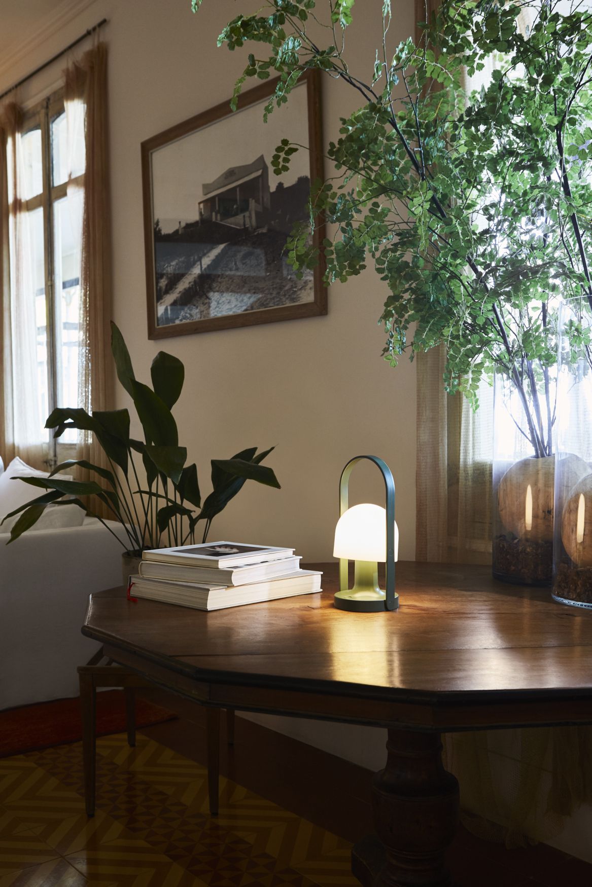 FollowMe LED Akkuleuchte von Marset in Terrakotta auf einem Holztisch mit Büchern und Pflanzen.