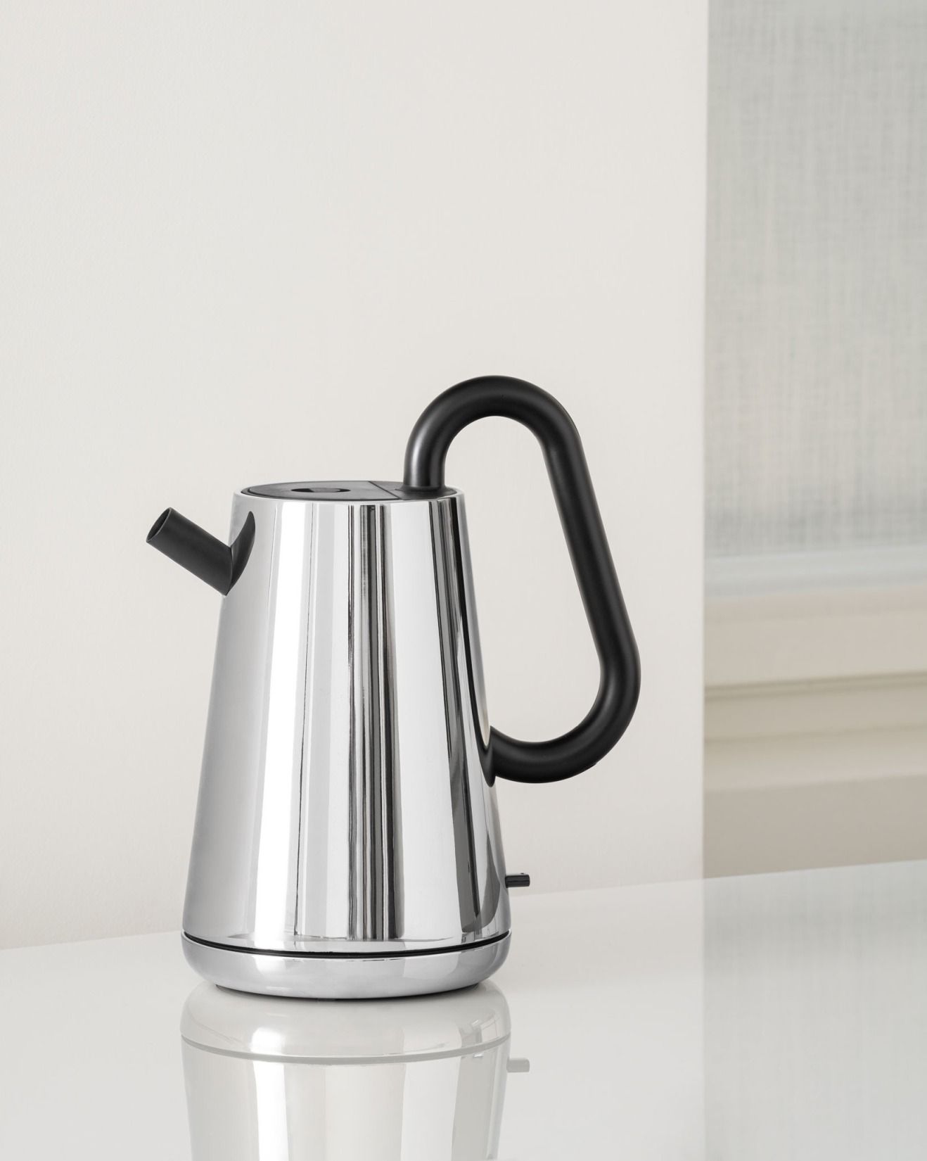 Alessi NE01 B Toru Wasserkocher aus Edelstahl mit schwarzem Griff auf weißer Oberfläche.
