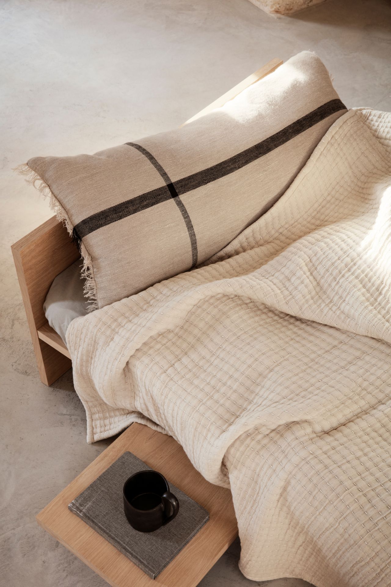 Detailaufnahme des Kona Bettes von Ferm Living mit Decke, Kissen und Nachttisch.