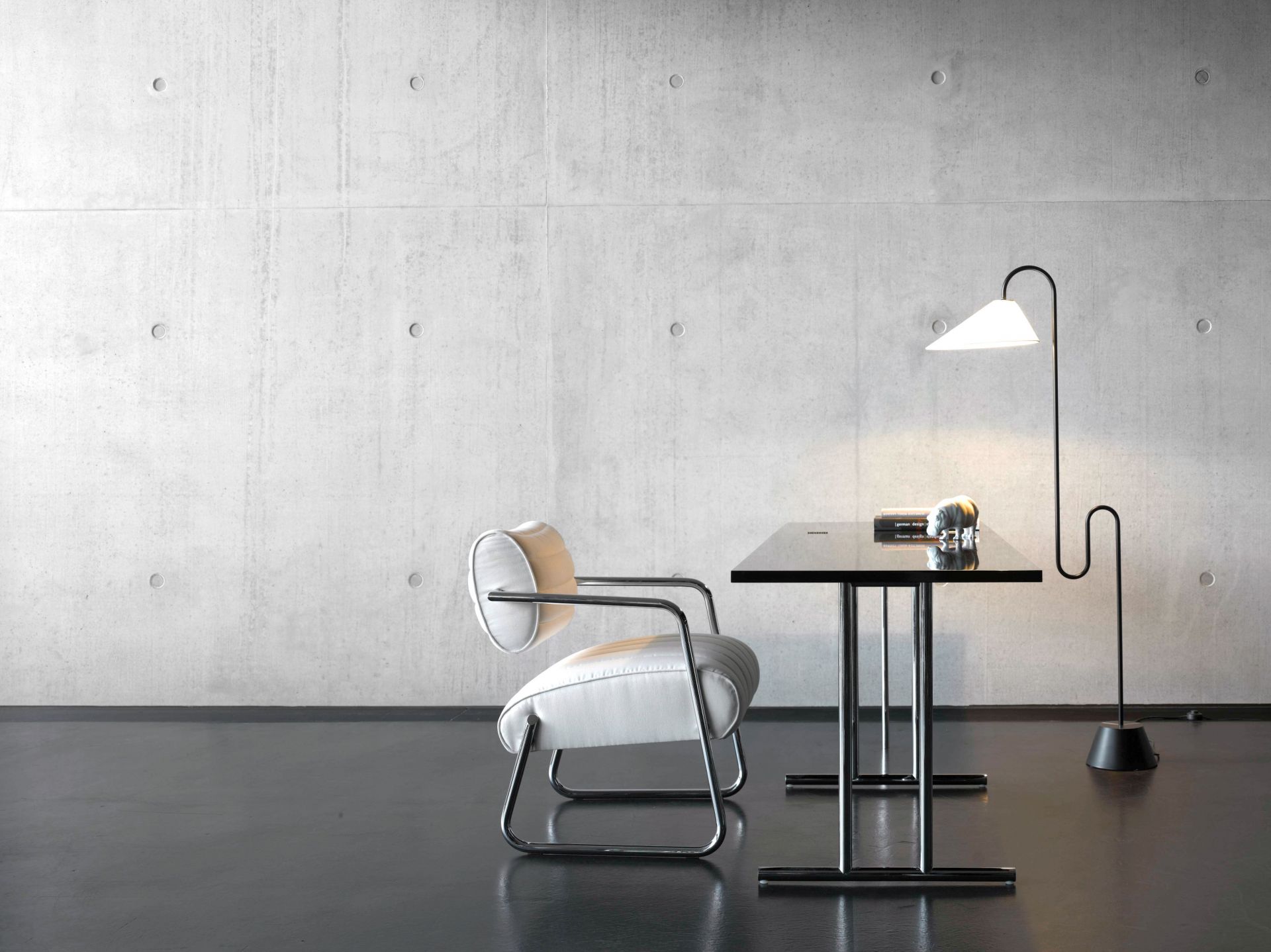 Lou Perou Ausklapptisch von ClassiCon mit Lampe und Sessel vor einer Betonwand, modernes Bürodesign.