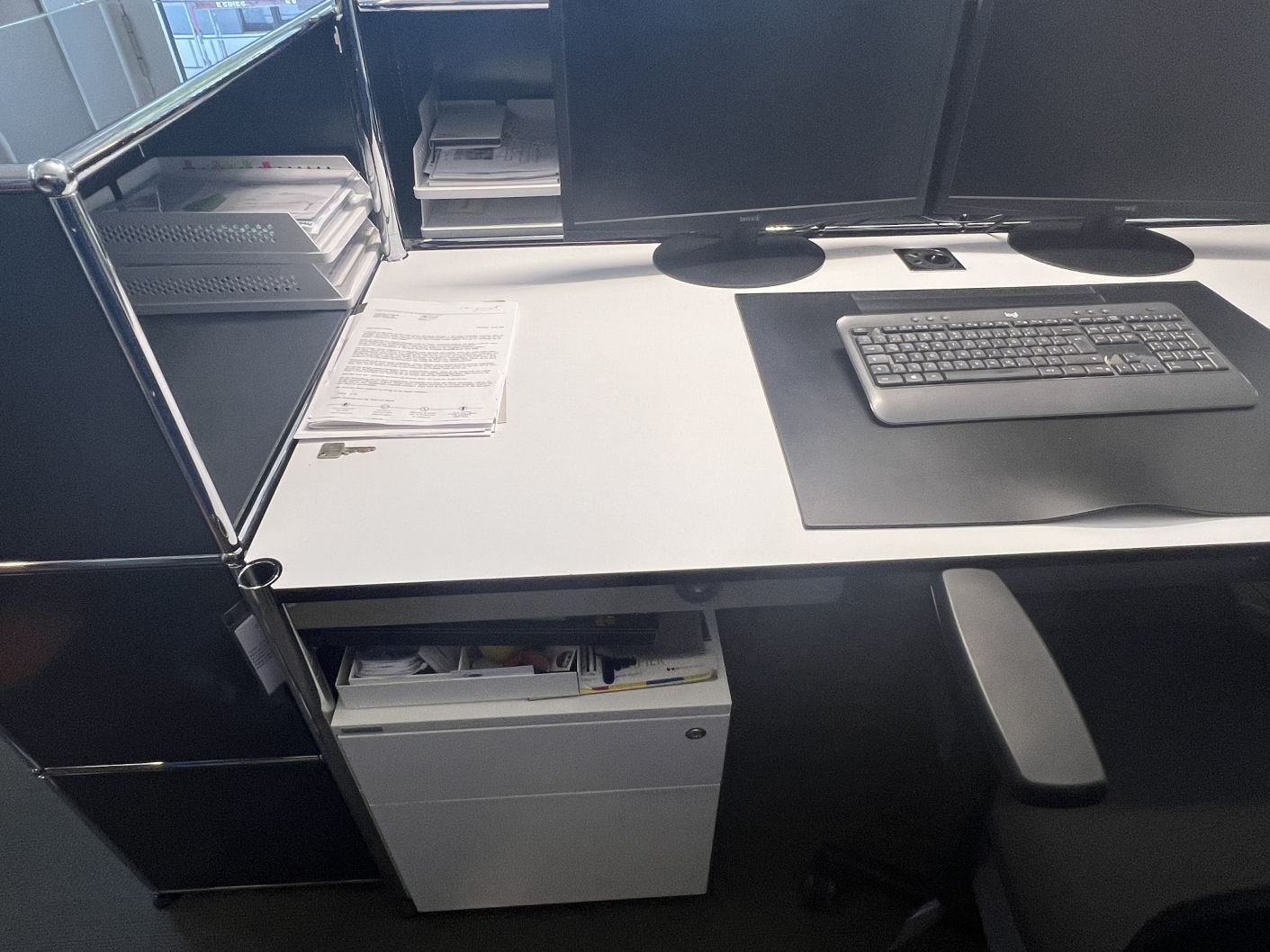 Detailaufnahme eines gebrauchten USM Haller Schreibtisches mit Monitoren, Tastatur und Büromaterial für ein modernes Büro.