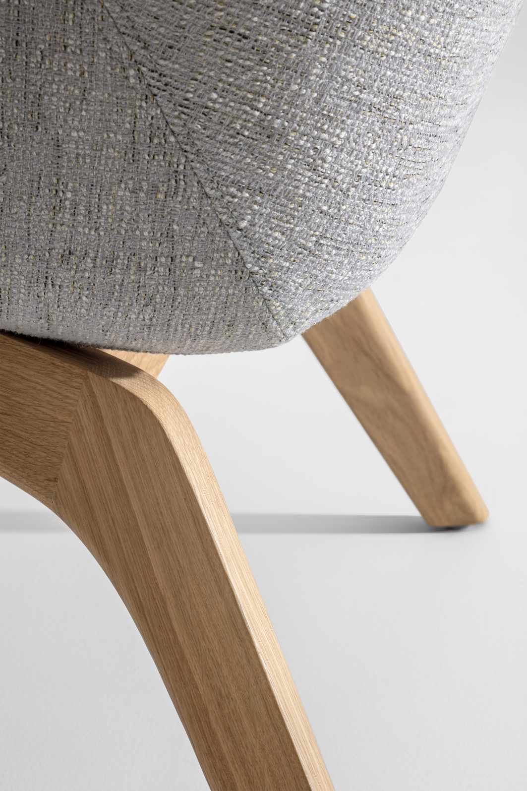 Detailaufnahme des Morph Lounge Chair Sessels mit grauem Stoffbezug und hellen Holzbeinen.