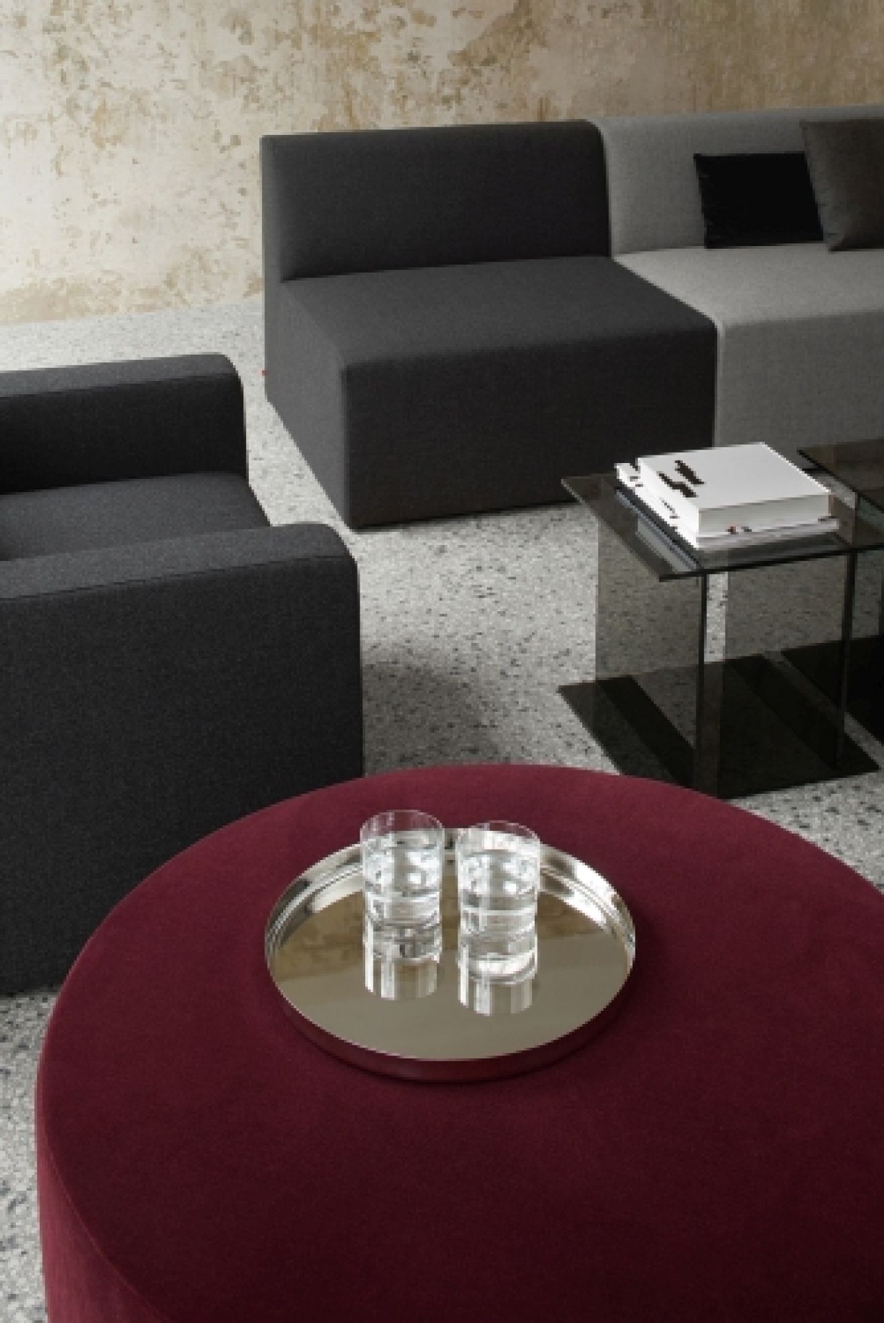 SF06 Kerman Modulsofa von e15 in Grau, kombiniert mit rotem Hocker und Glasbeistelltisch.