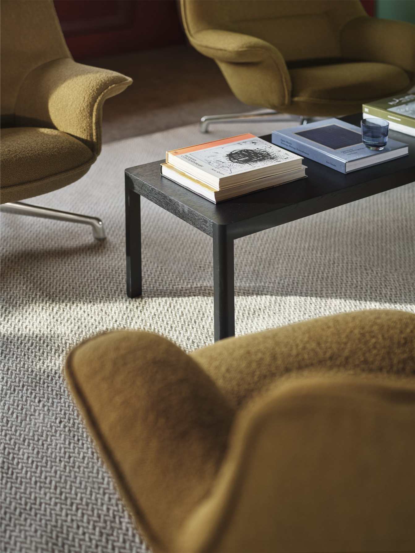 Nahaufnahme eines braunen Muuto Doze Lounge Sessels mit Tisch und Büchern.