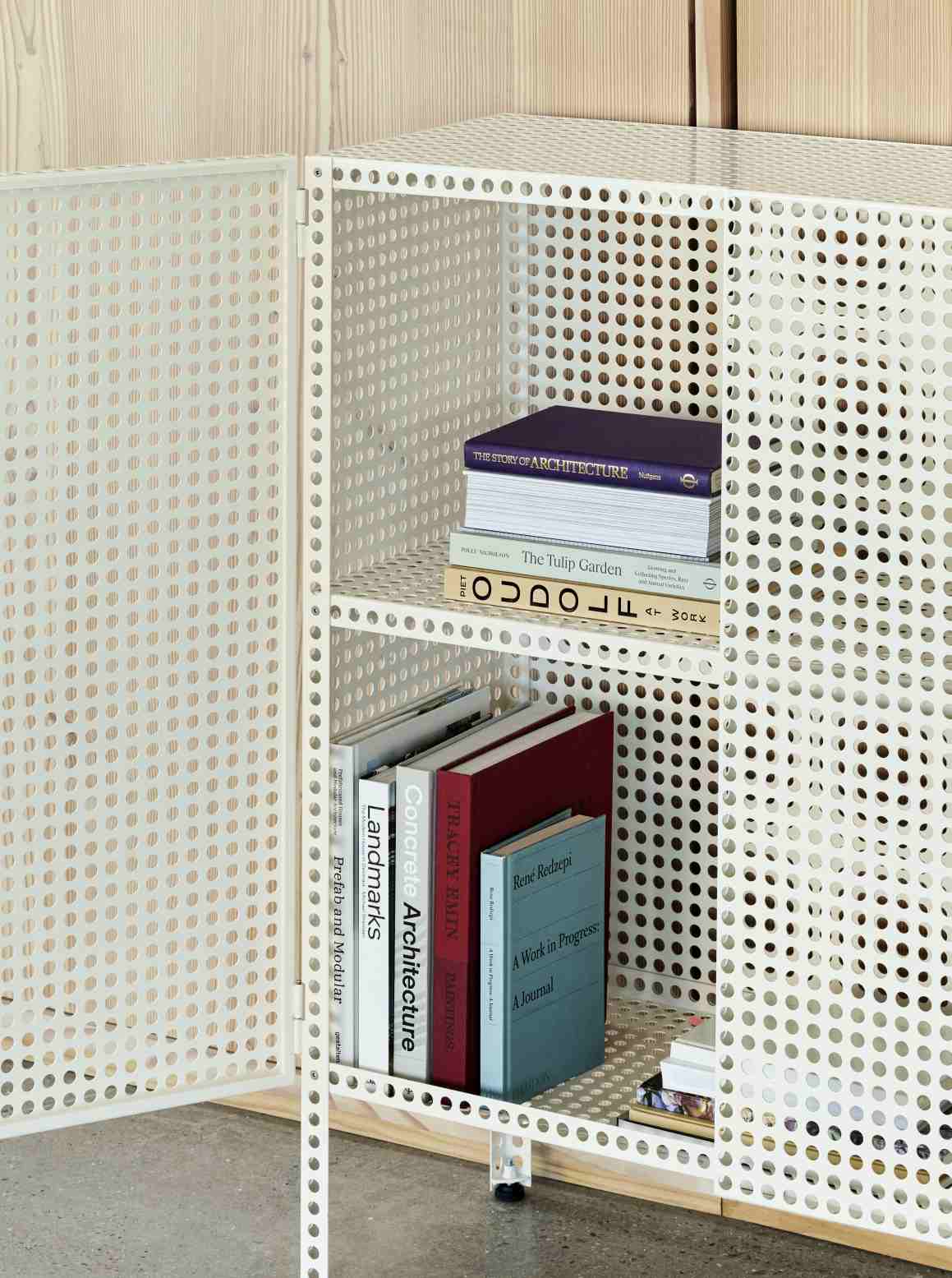 Weißes Hay Sideboard mit perforierter Metalltür und Regalen, gefüllt mit Büchern, modernes Möbeldesign.