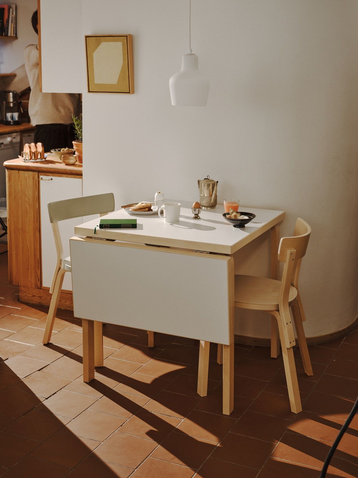 Aalto Table foldable Klapptisch Artek mit Frühstücksgedecken und zwei Holzstühlen in einem hellen Raum.