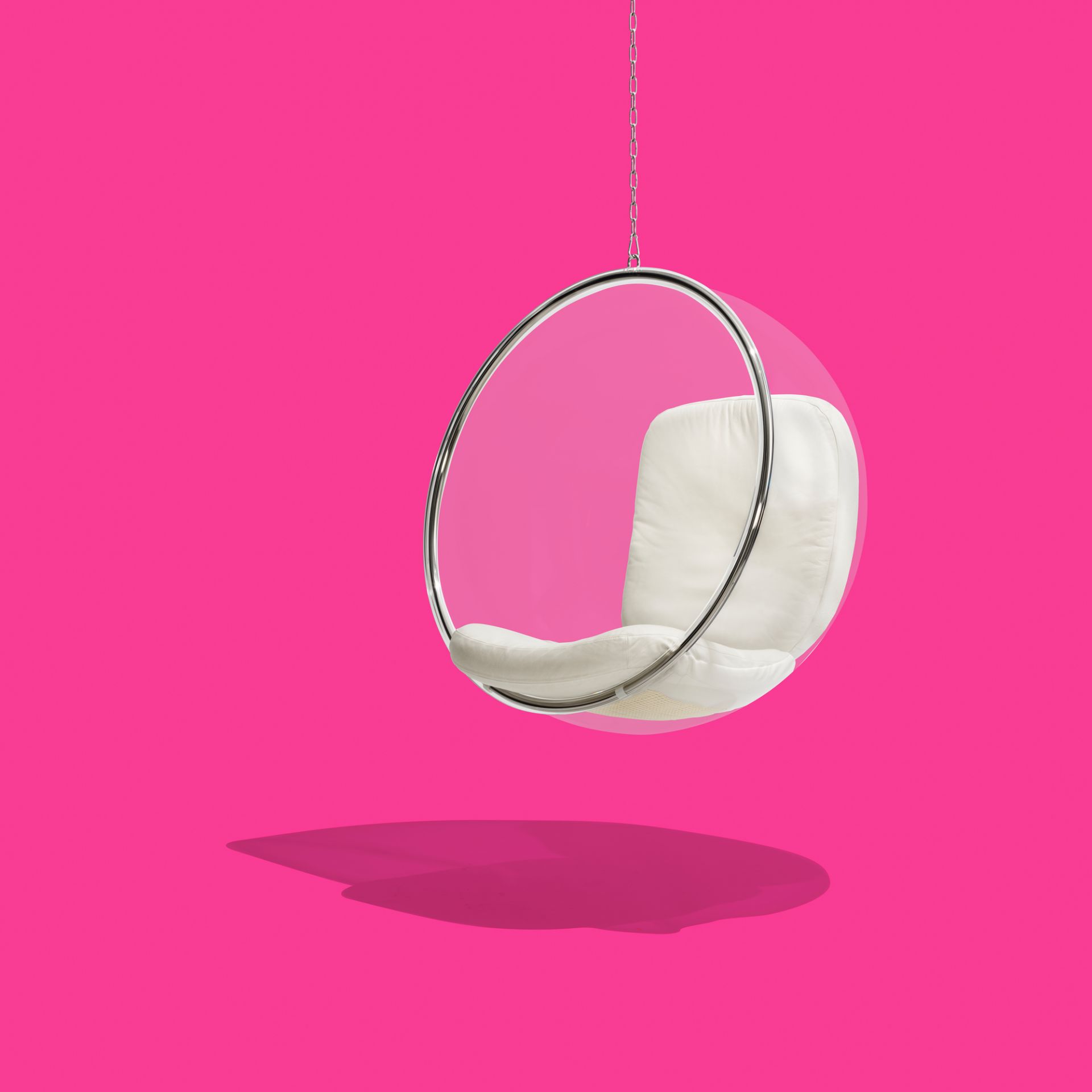 Bubble Chair: Transparenter Hängesessel mit weißen Kissen, aufgehängt an einer Kette vor pinkfarbenem Hintergrund.