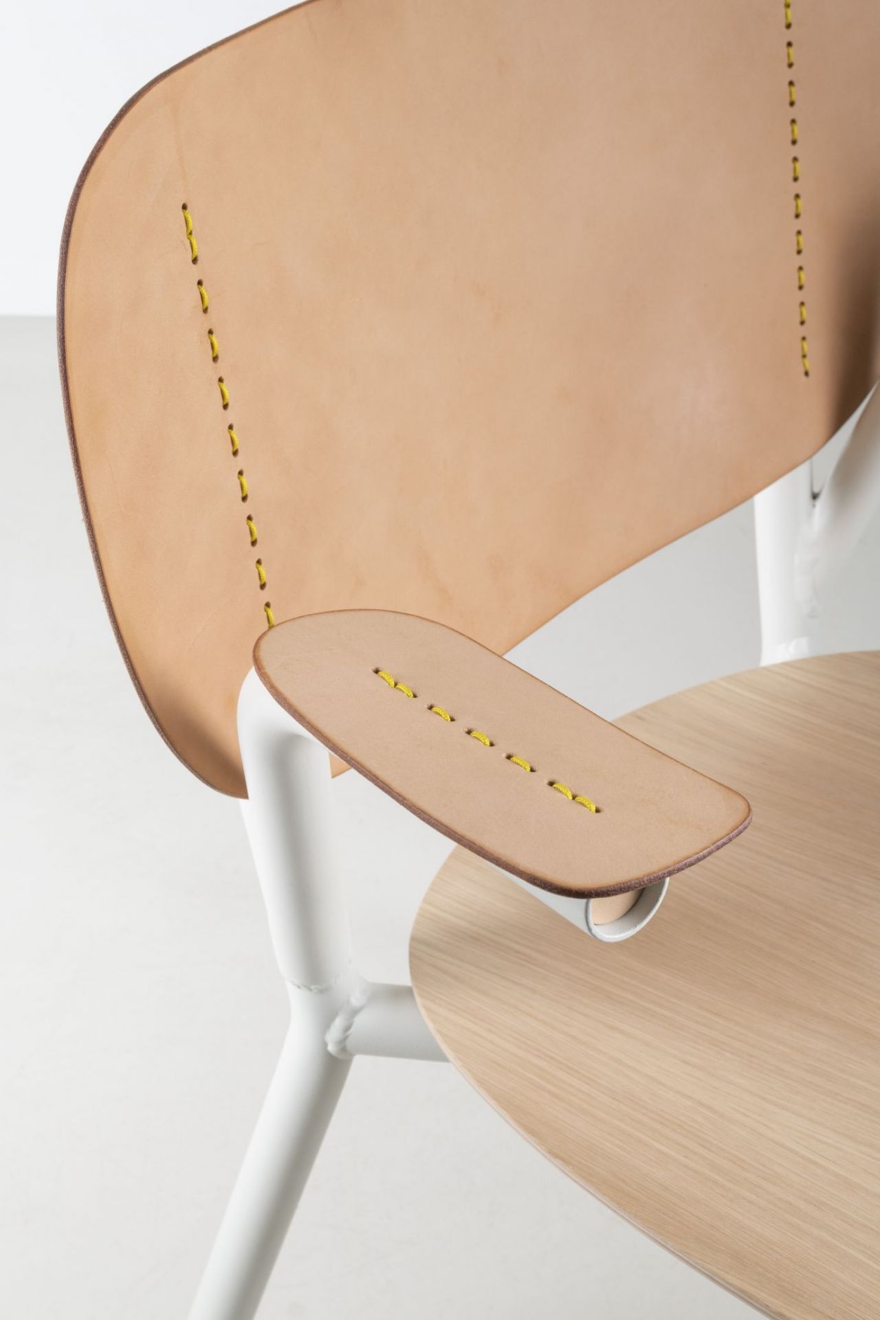 Detailaufnahme des Emil Rosi Armchair Stuhls: Leder, gelbe Ziernähte, helle Holzoberfläche und weißes Metallgestell.