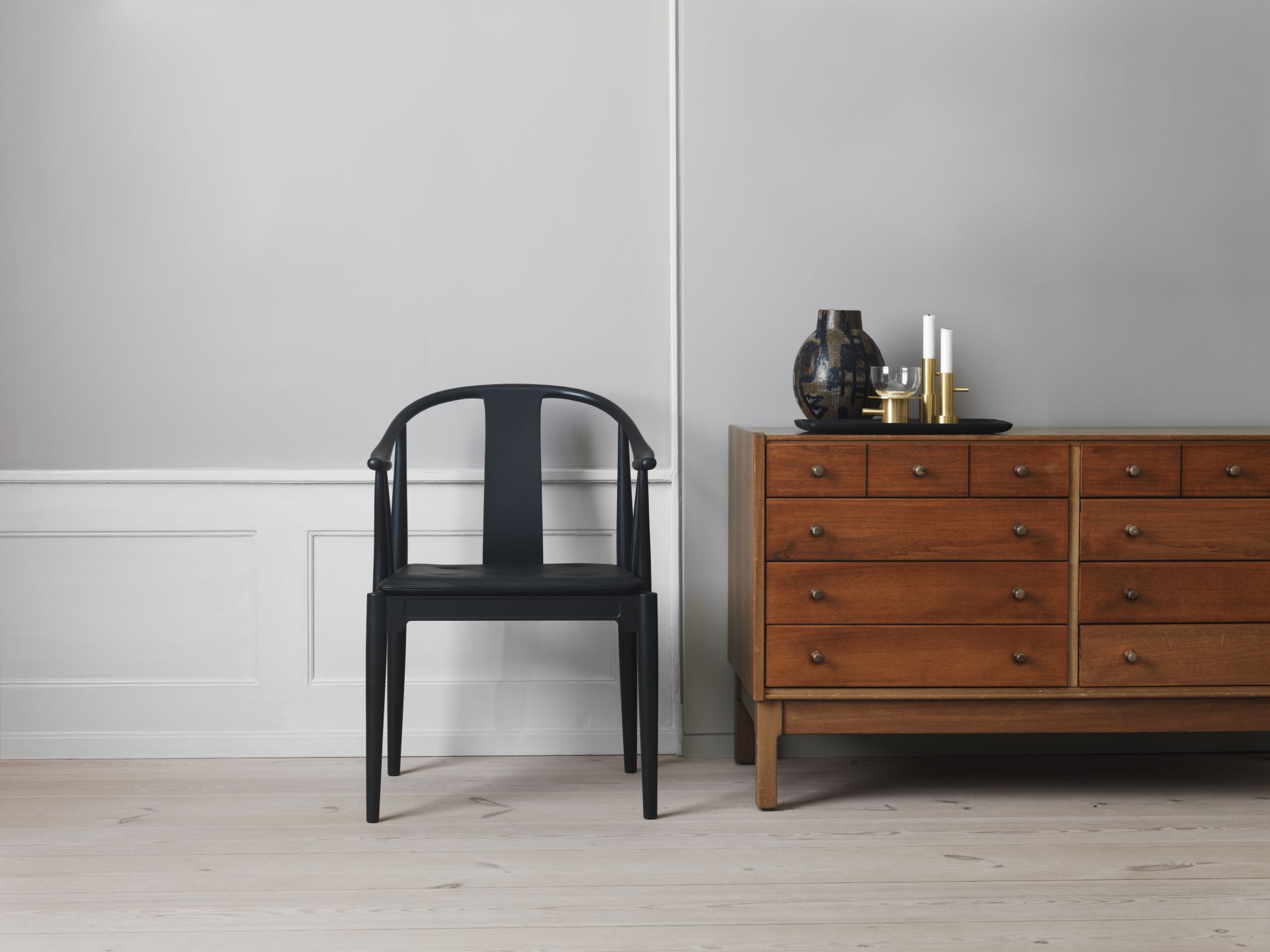 Schwarzer China Chair Stuhl von Fritz Hansen neben einer Holzkommode mit dekorativen Wohnaccessoires.