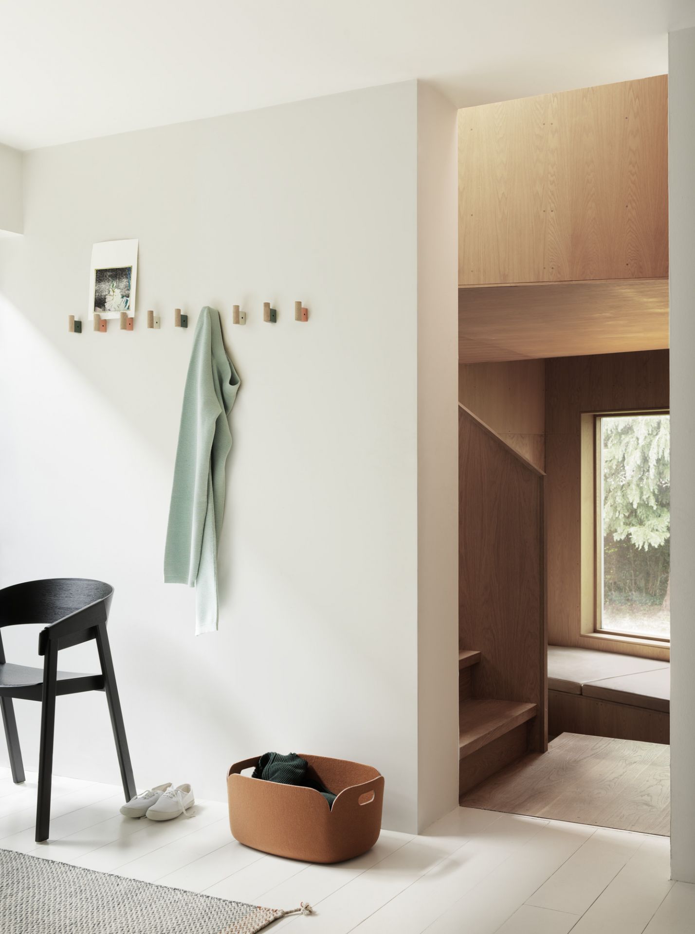 Schwarzer Cover Chair Stuhl von Muuto in minimalistischem Flur mit Garderobe, Korb und Treppenaufgang.