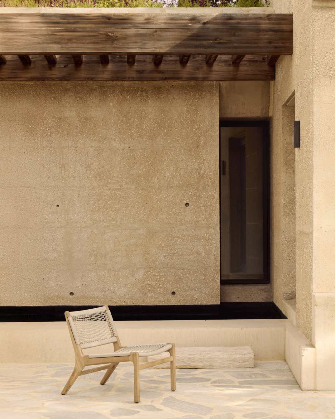 Jack Woven Outdoor Loungesessel von Ethnicraft: Teakholz Gartenstuhl mit beiger Kordel vor beiger Hauswand.