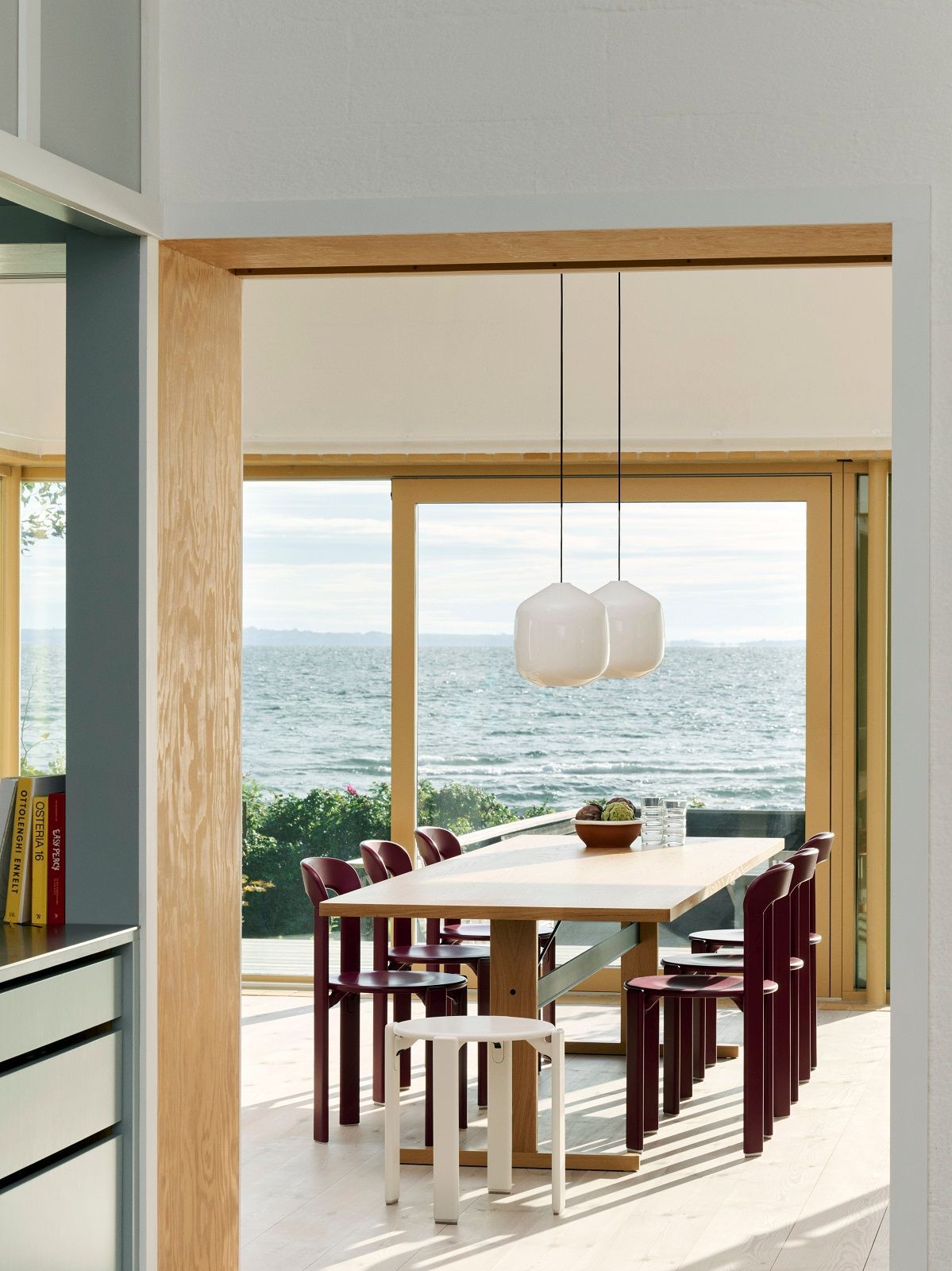 Zwei weiße Aspekt Buoy Glass Pendelleuchten von Hay über einem Esstisch mit Meerblick.