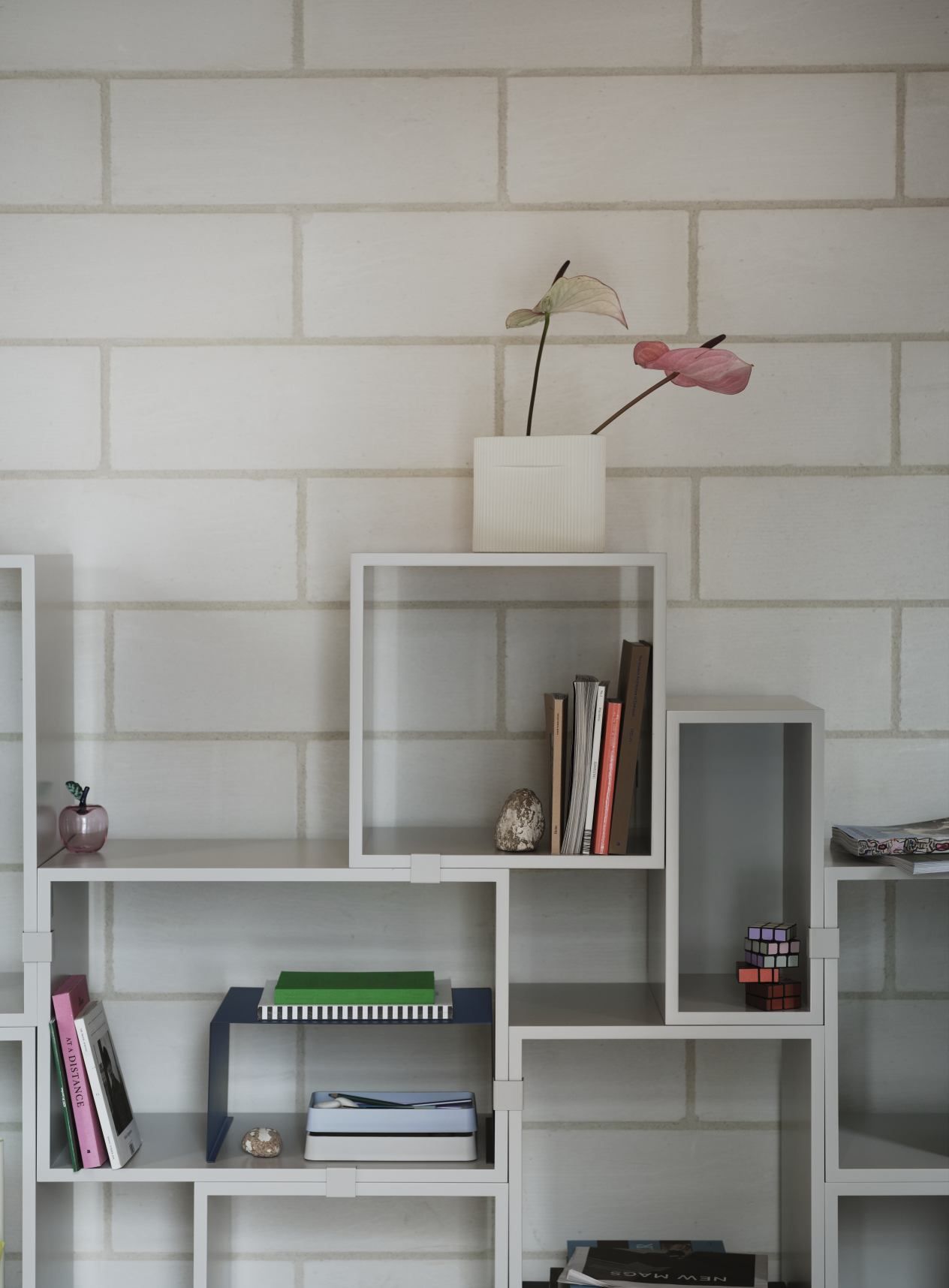 Weißes Muuto Stacked Storage Regalsystem 2.0 mit Deko vor einer weißen Ziegelwand. Modernes Regalsystem für Wohnzimmer.